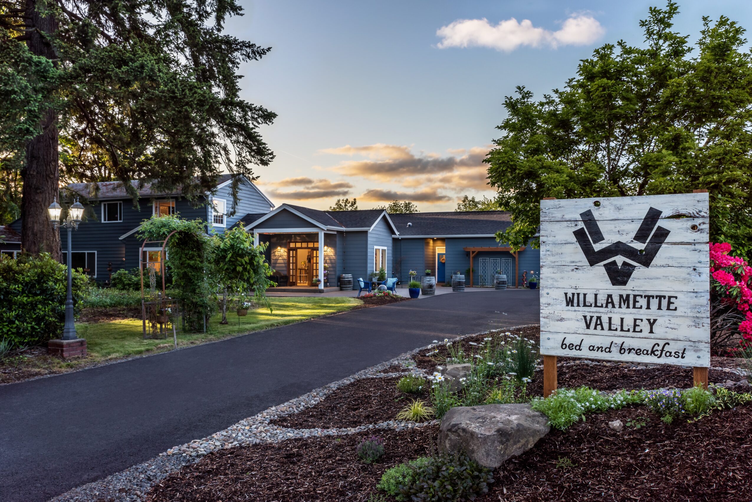 Blue building with a sign reading Willamette Valley Bed and Breakfast, surrounded by trees and a paved driveway.