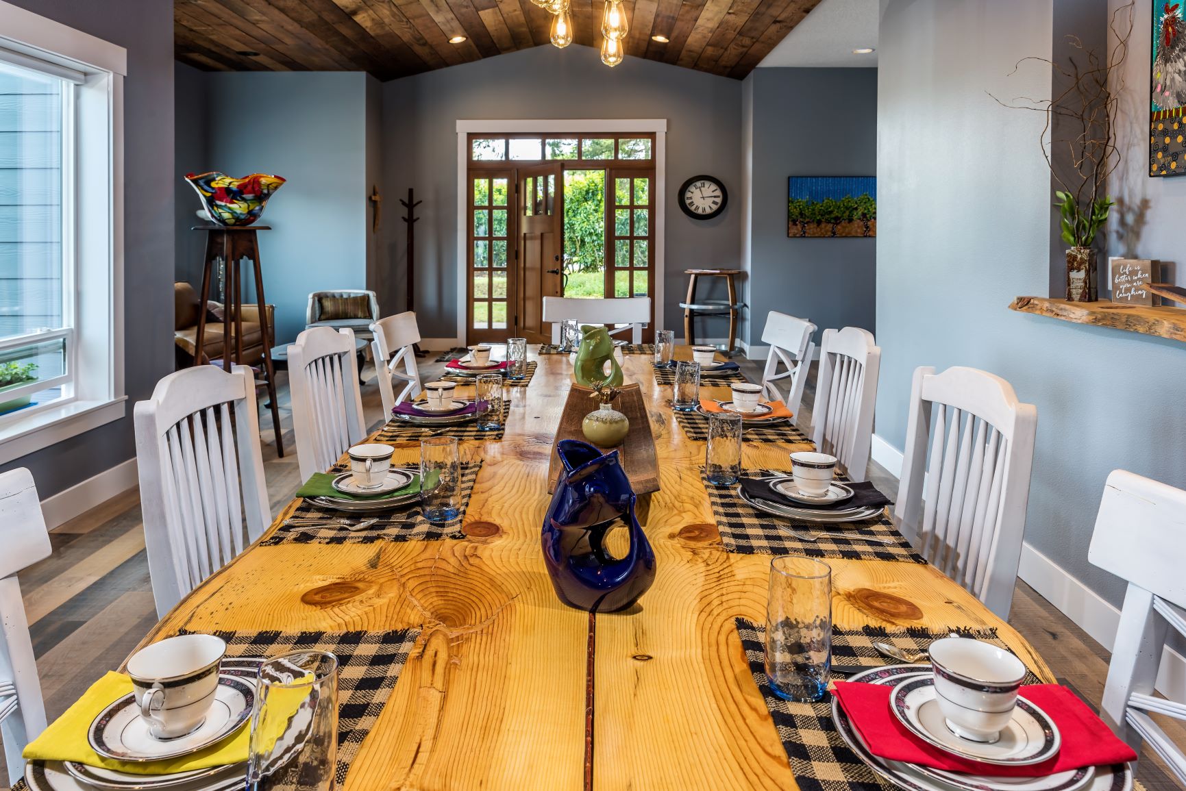 Dining room with a long wooden table, white chairs, and a view of a door with glass panels, decorated with vases and tableware.