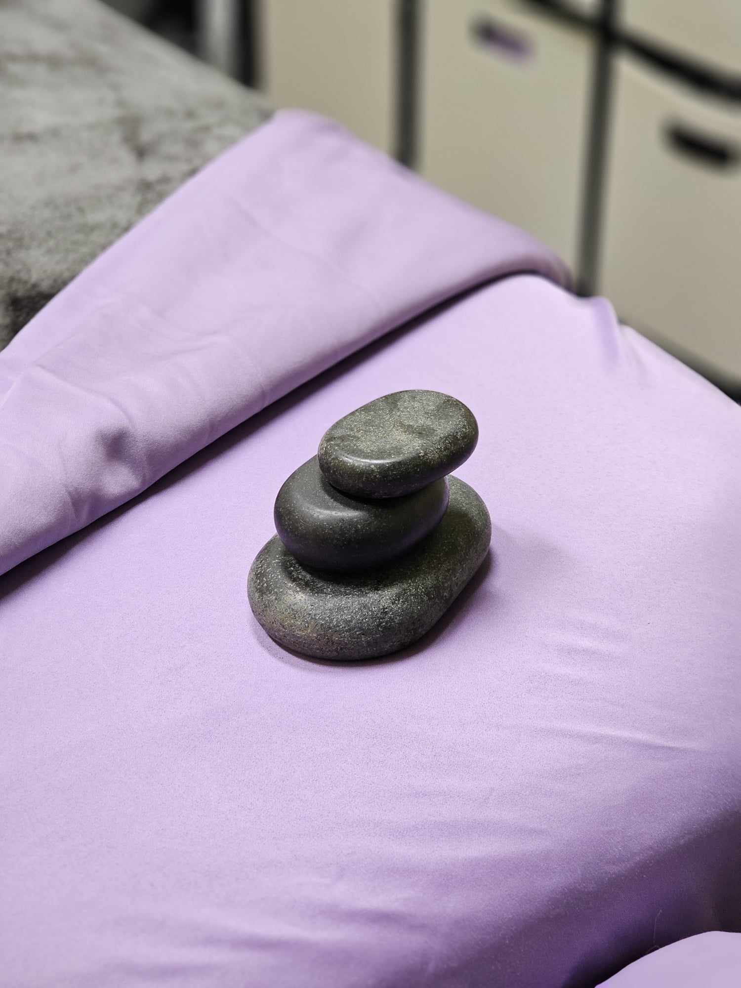 Stack of five smooth, rounded stones on a purple fabric surface with a blurred background.