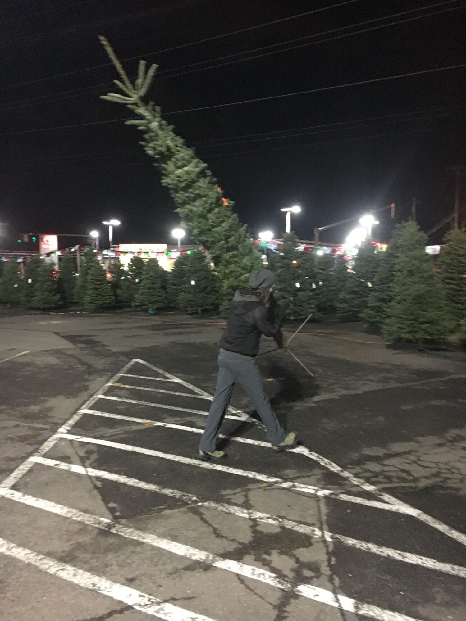 Person walking in a parking lot at night with trees and lights in the background.