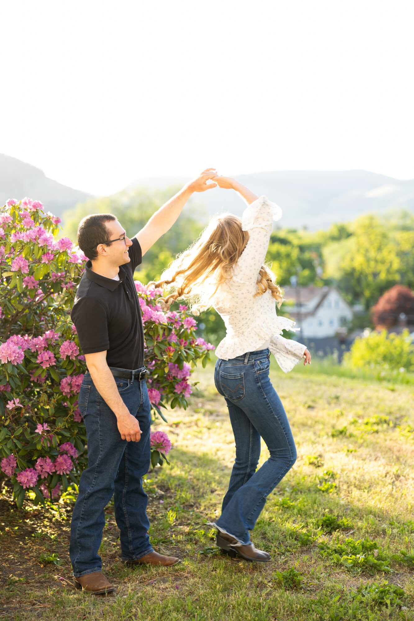 Two people dancing outdoors near pink flowers, with a scenic landscape in the background, bright sunlight, and clear sky.