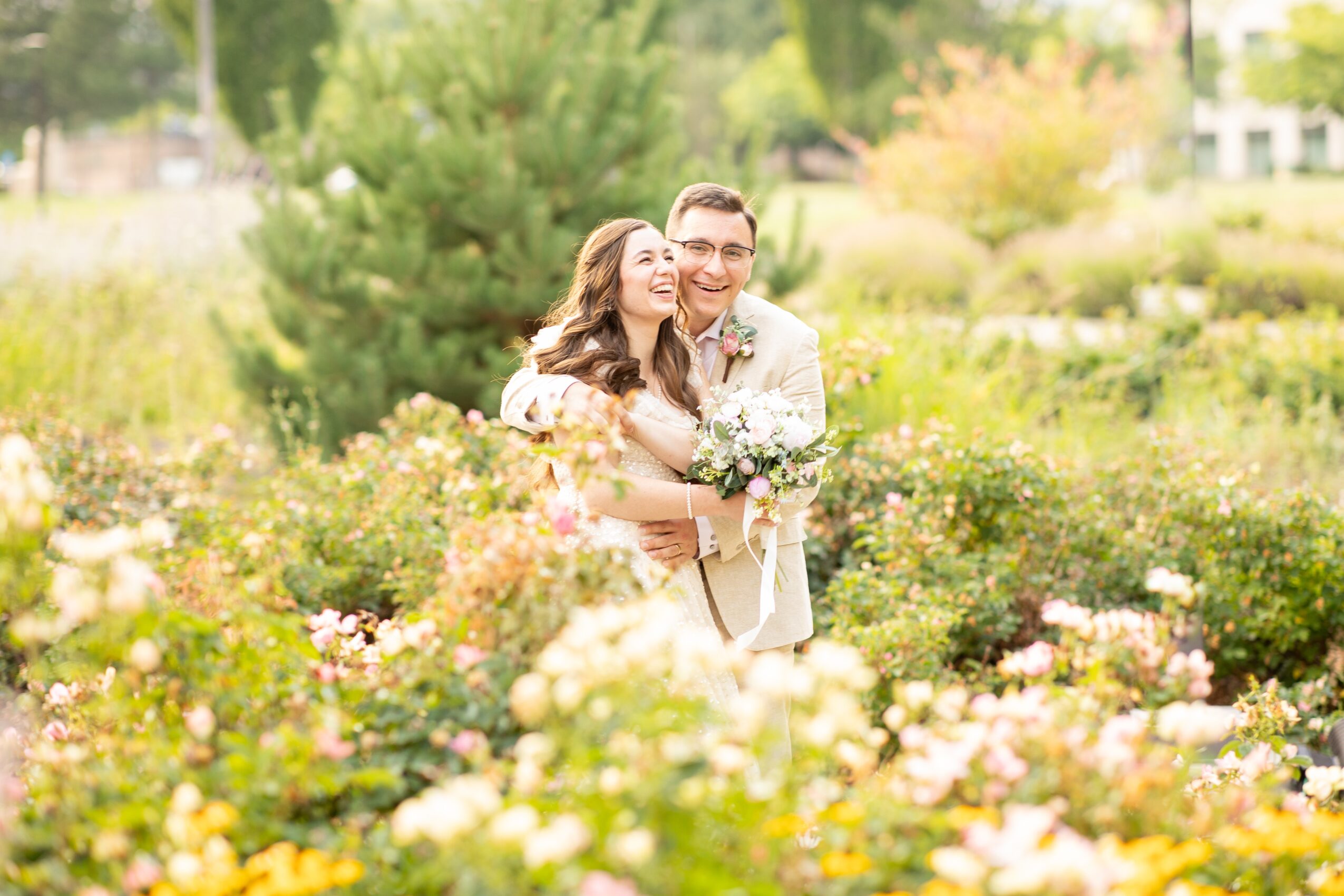 A couple hugging in a garden with colorful flowers and greenery, smiling happily.