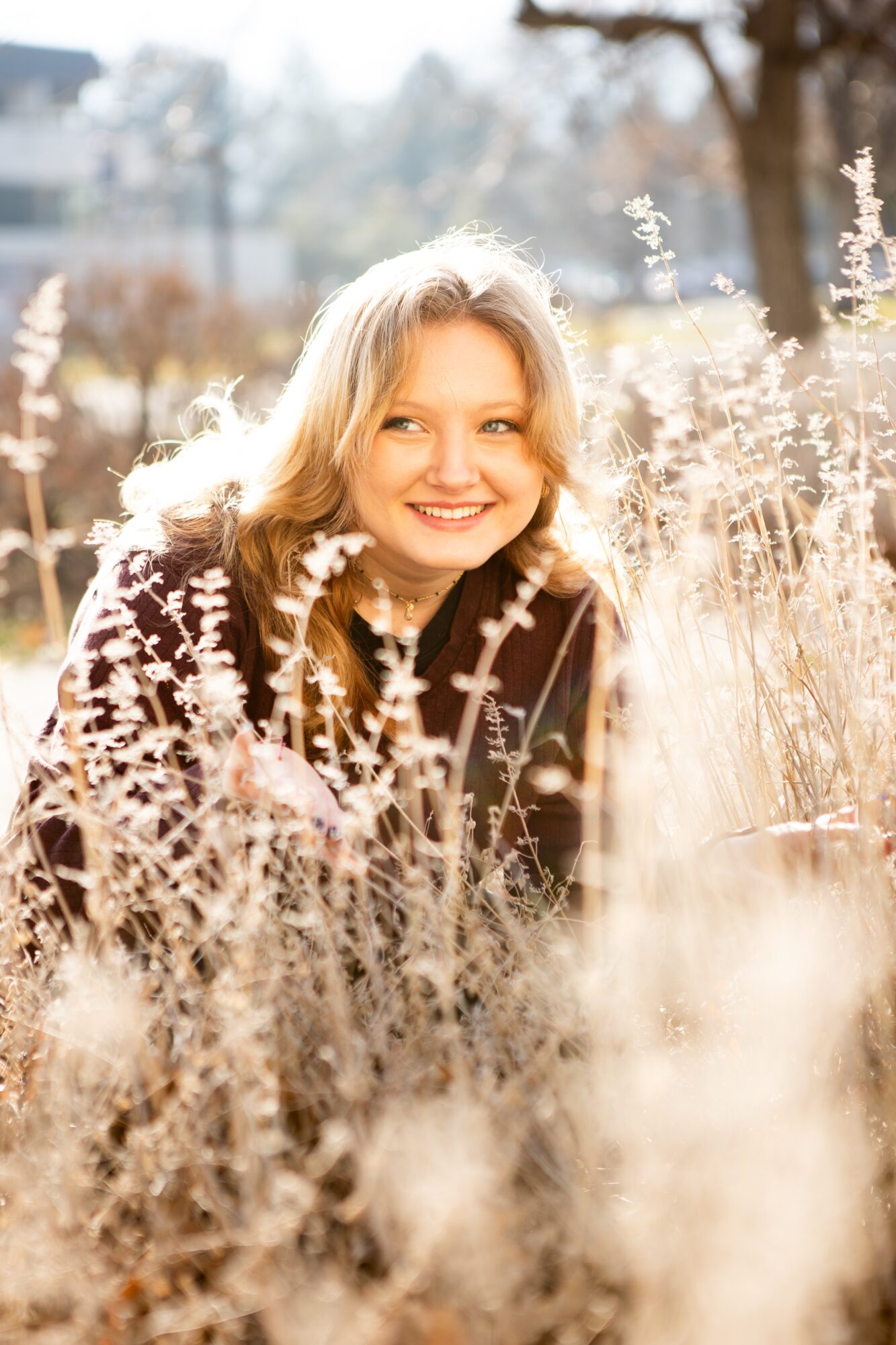 Smiling woman with blonde hair among tall, dry grasses outdoors on sunny day.