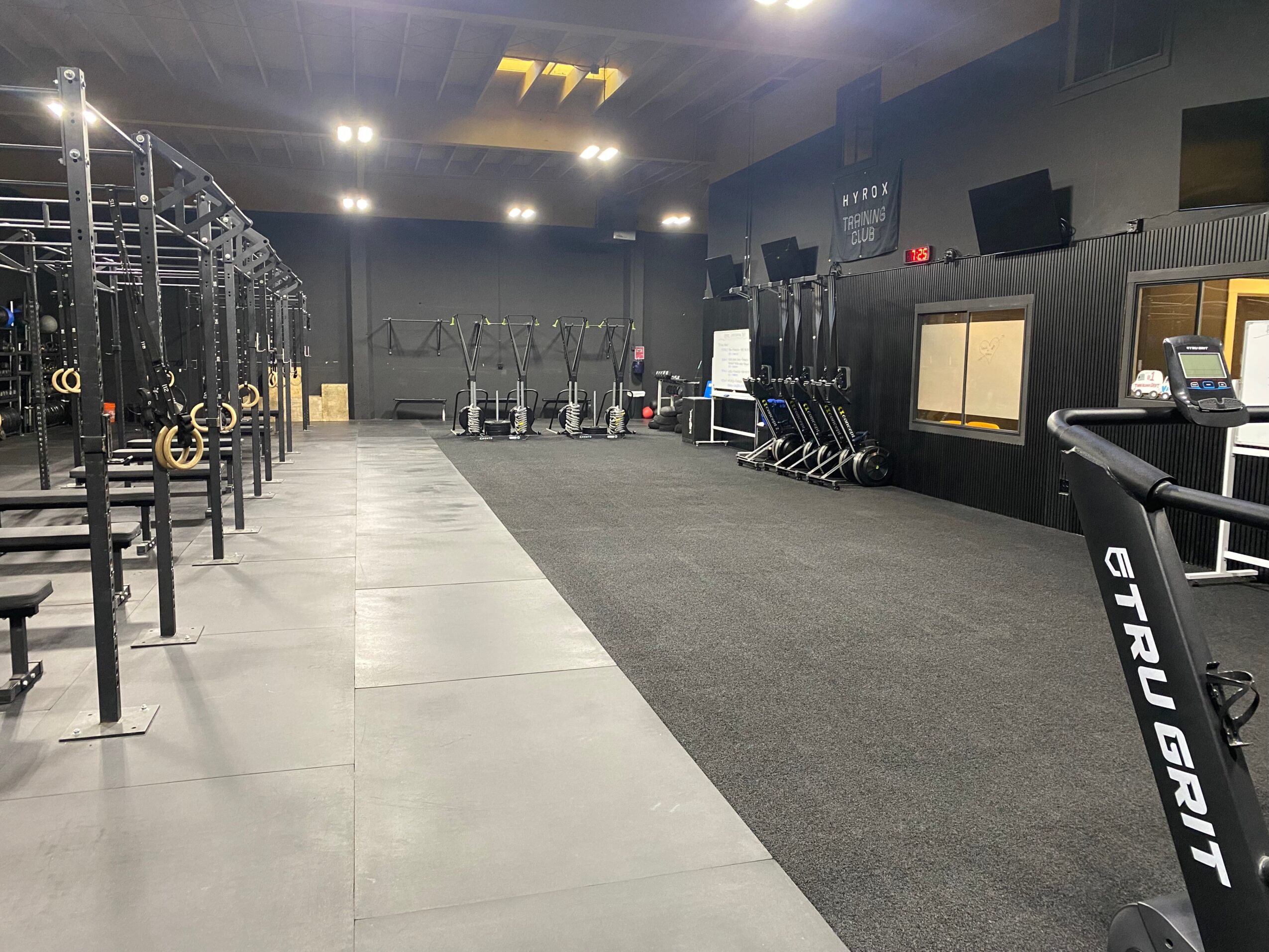 Empty gym with workout equipment, black walls, and a mix of concrete and carpeted flooring.