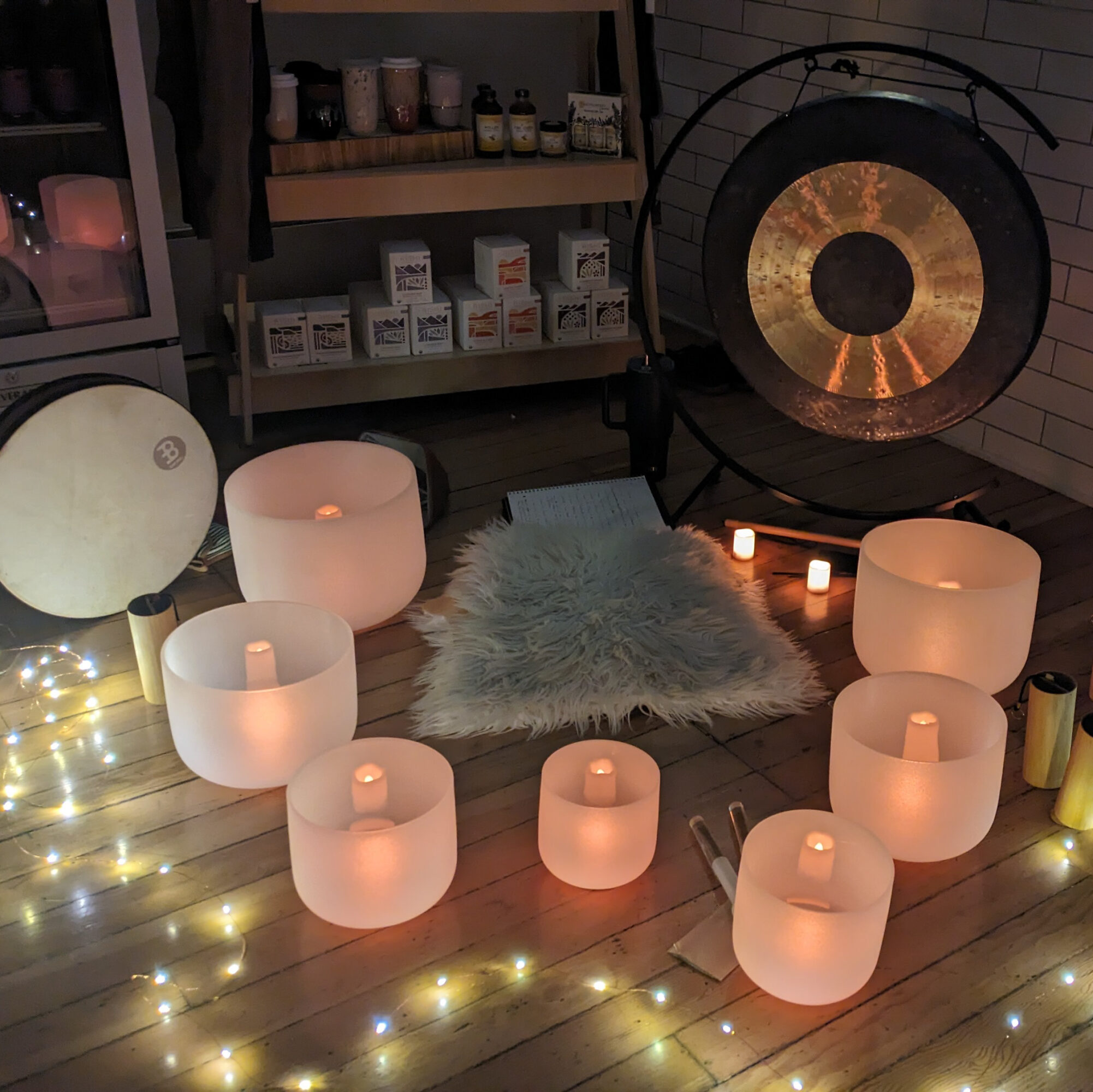 Room with candles, fairy lights, a fluffy rug, and a large gong on a wooden floor, creating a cozy atmosphere.