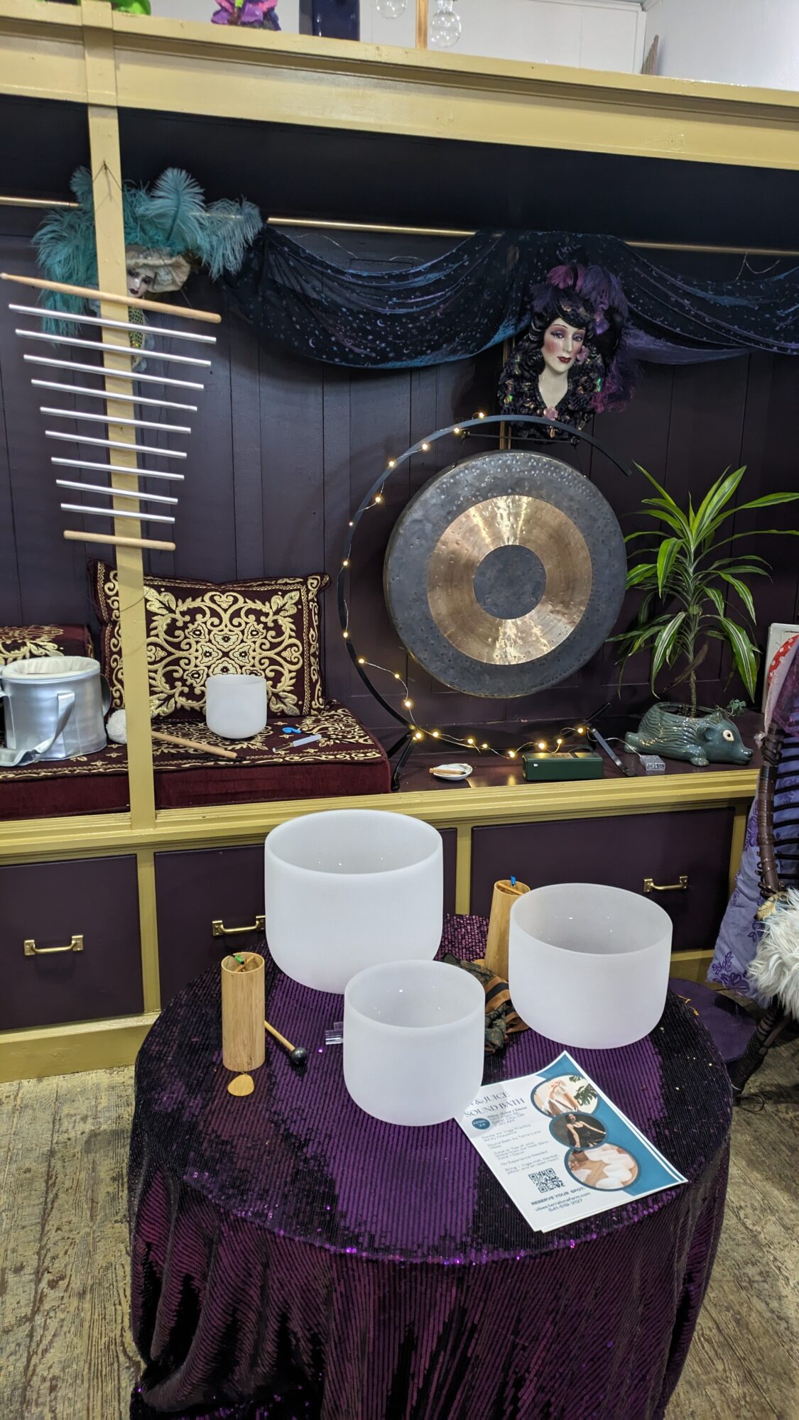 Musician playing gong with decorative background and plants, on a table with white bowls and a booklet.
