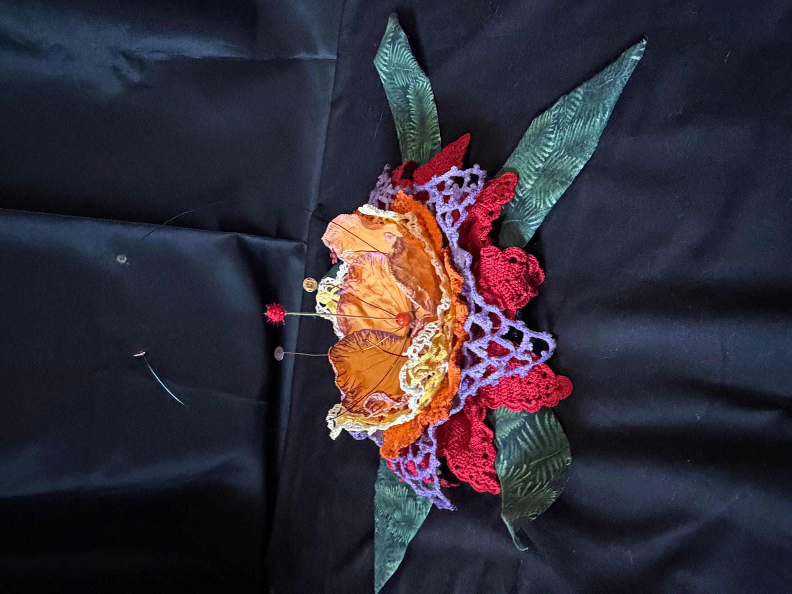 Colorful embroidered flower with green leaves on black fabric.