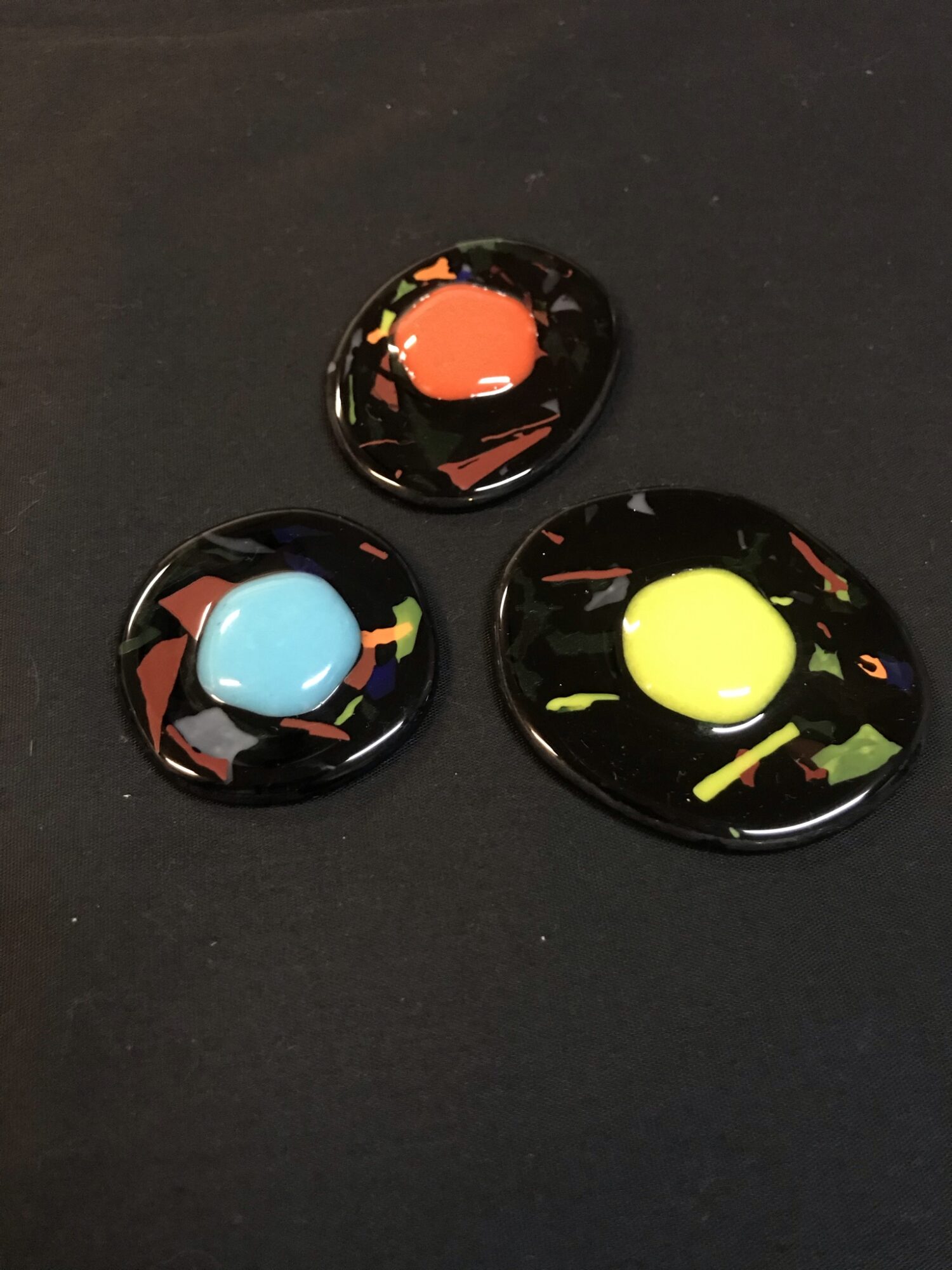 Three glass marbles with colorful patterns on a black surface, one orange, one blue, and one yellow.