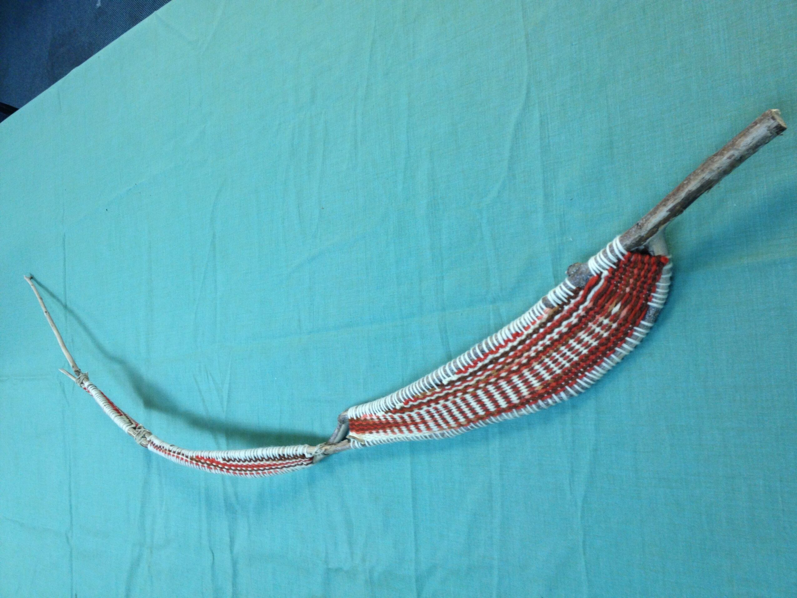 A curved, decorated bow with a wooden handle and a string, resting on a blue surface.