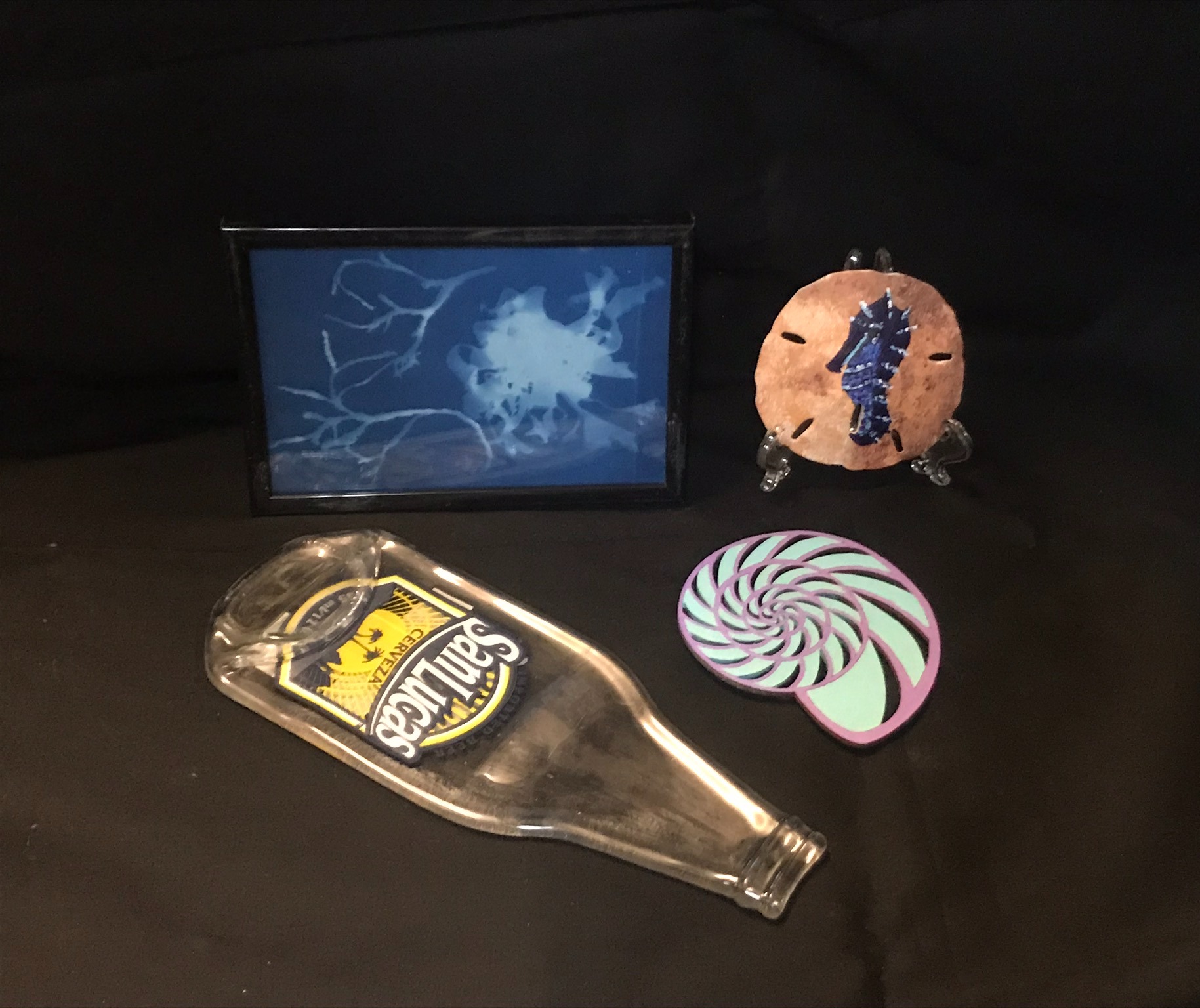 Four objects: framed lightning image, plush seahorse, glass bottle with a label, and a colorful spiral sticker, on a black surface.