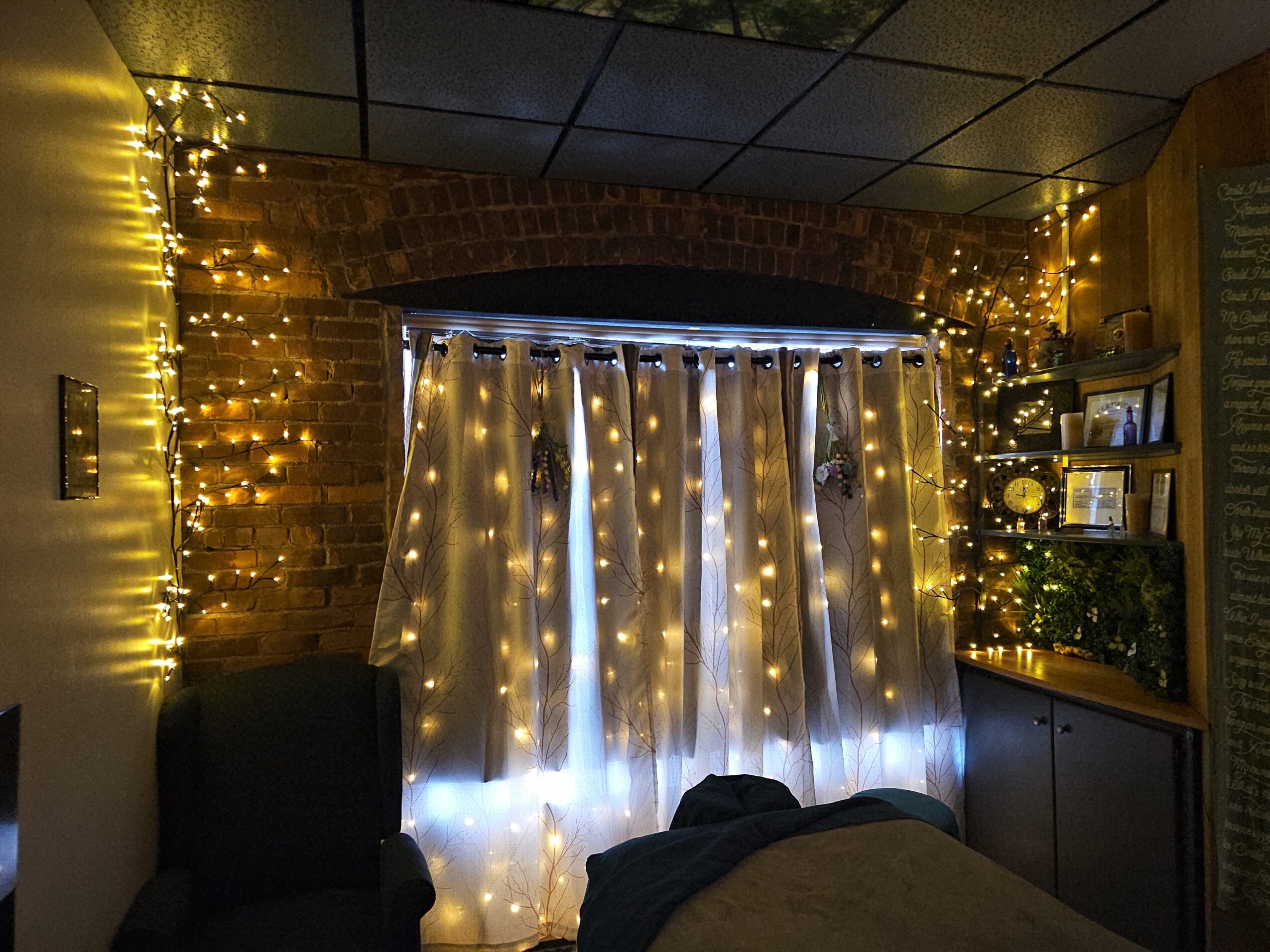 Curtain with string lights hanging in front of a window, decorated with fairy lights on brick wall, cozy indoor setting.