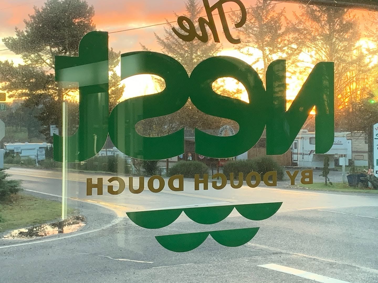 Reflected view of a sign with the word 'mash' and 'by borough dough' in a window, with trees and street scene outside