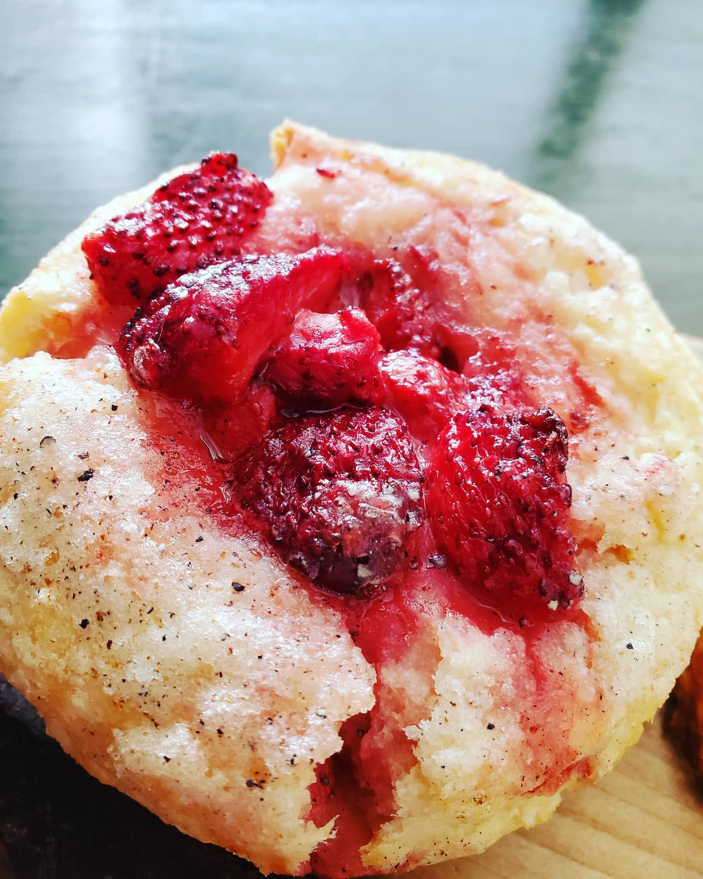 Close-up of a muffin topped with red berries and berry sauce, on a wooden surface, with a blurred background.