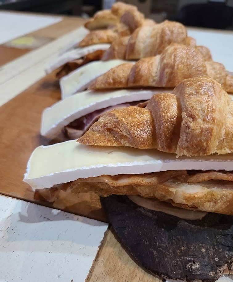 Croissant sandwiches with cheese and meat on a wooden board, viewed from the side.