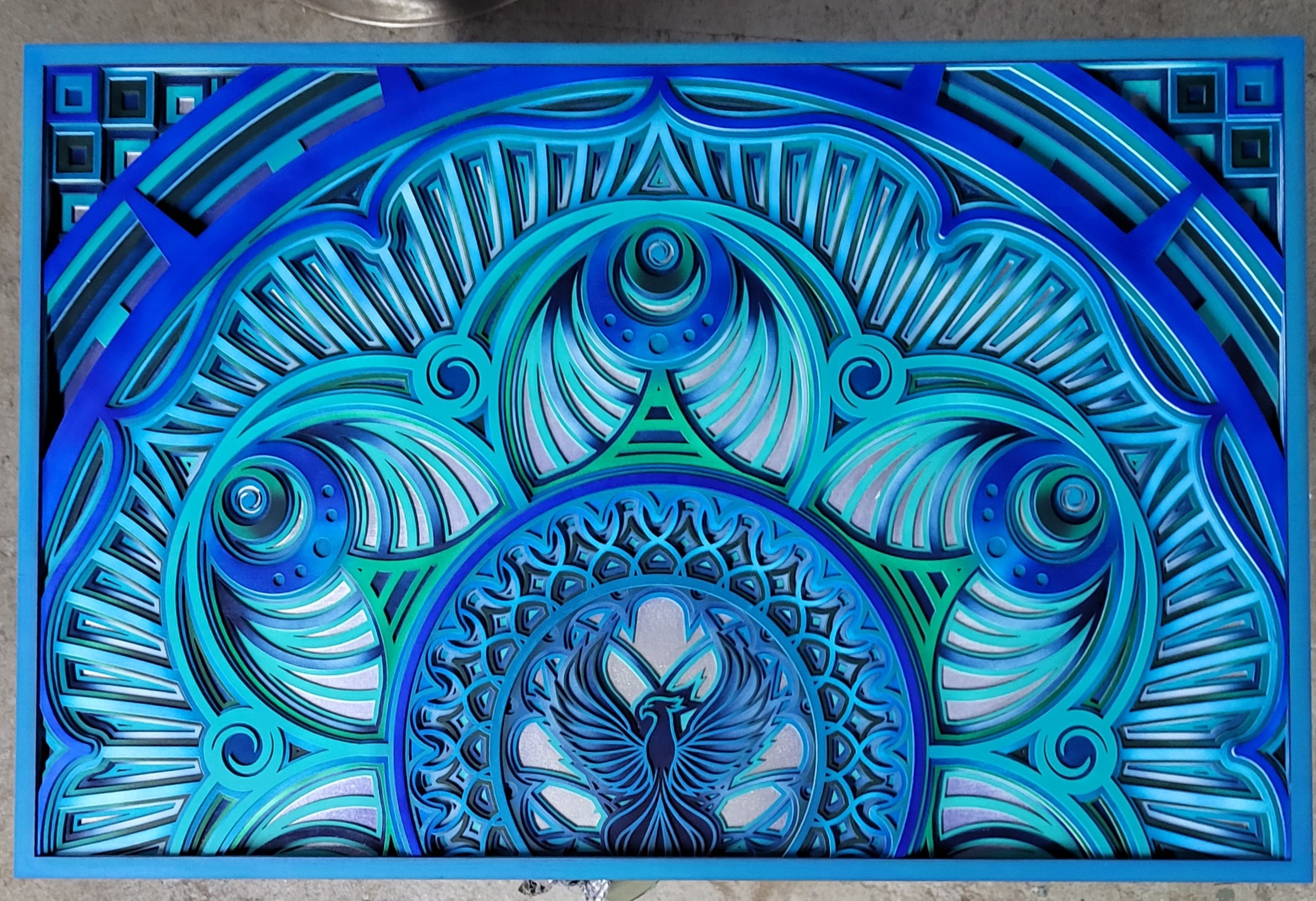 Intricate blue geometric pattern with circular and radiating elements, symmetrical design, and a central figure resembling a stylized bird or insect.