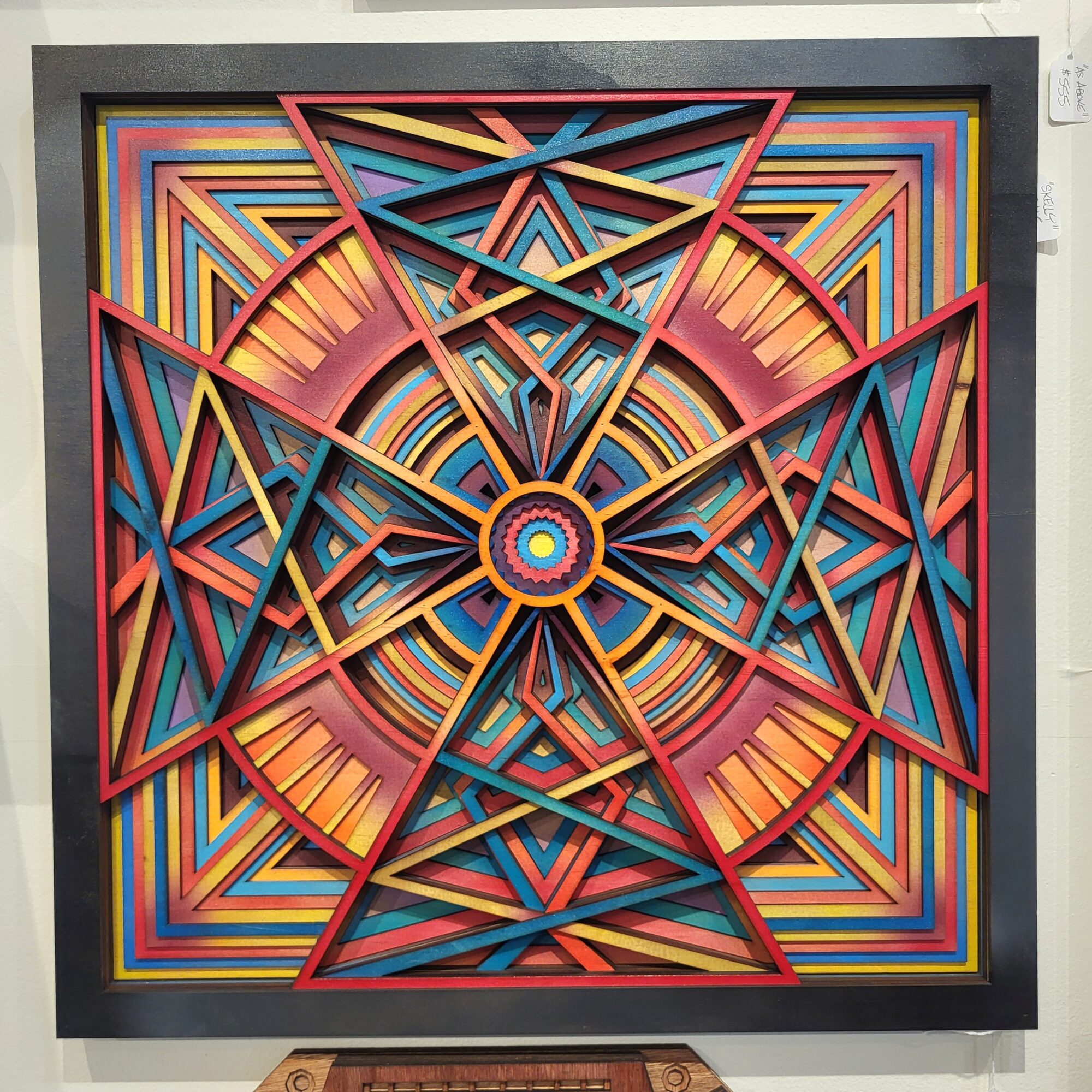 Colorful geometric artwork with overlapping triangles and concentric patterns, vibrant colors including red, blue, yellow, and orange, framed in black.