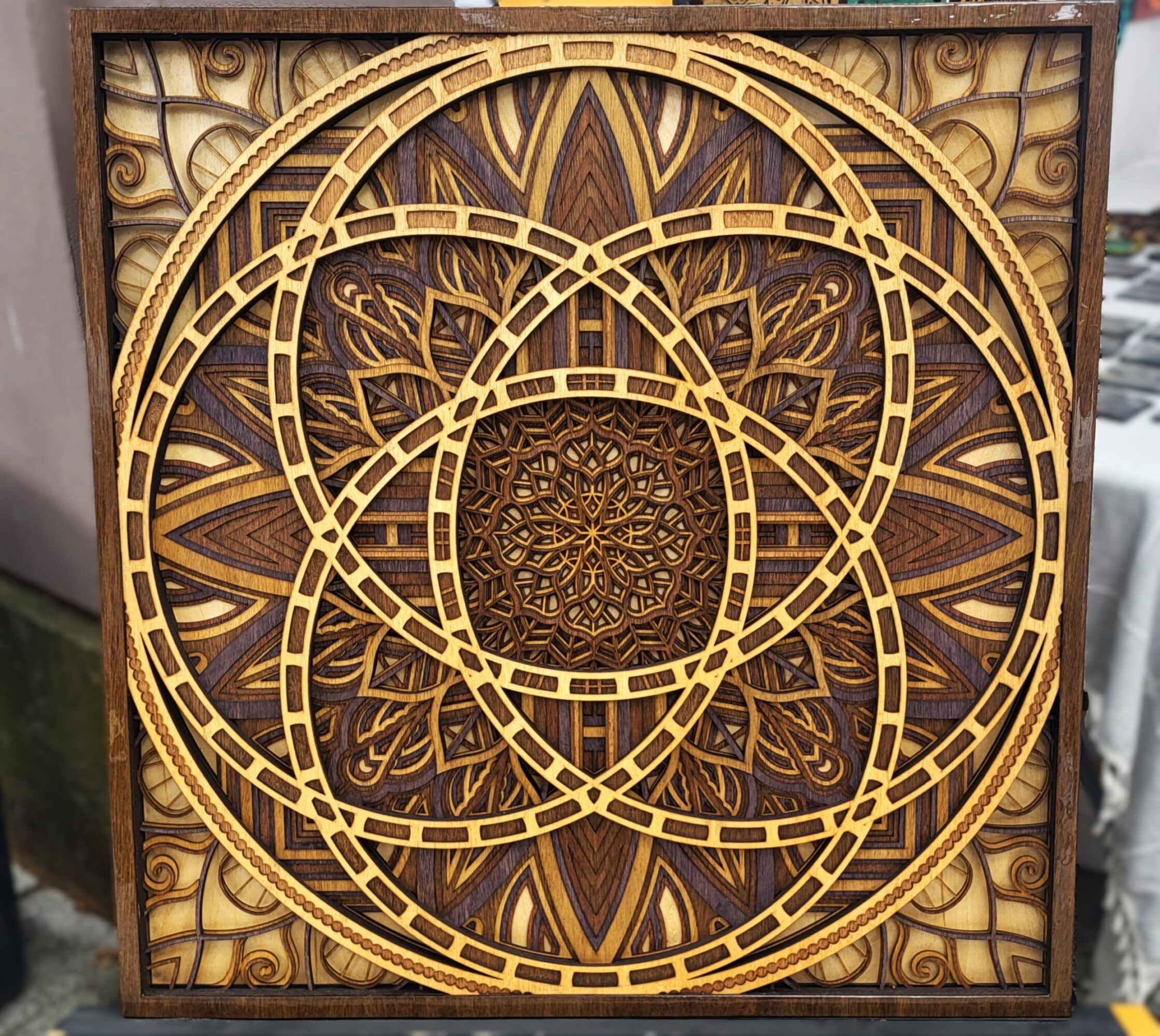 Decorative wooden wall art with intricate geometric patterns and overlapping circles, framed in a square shape.