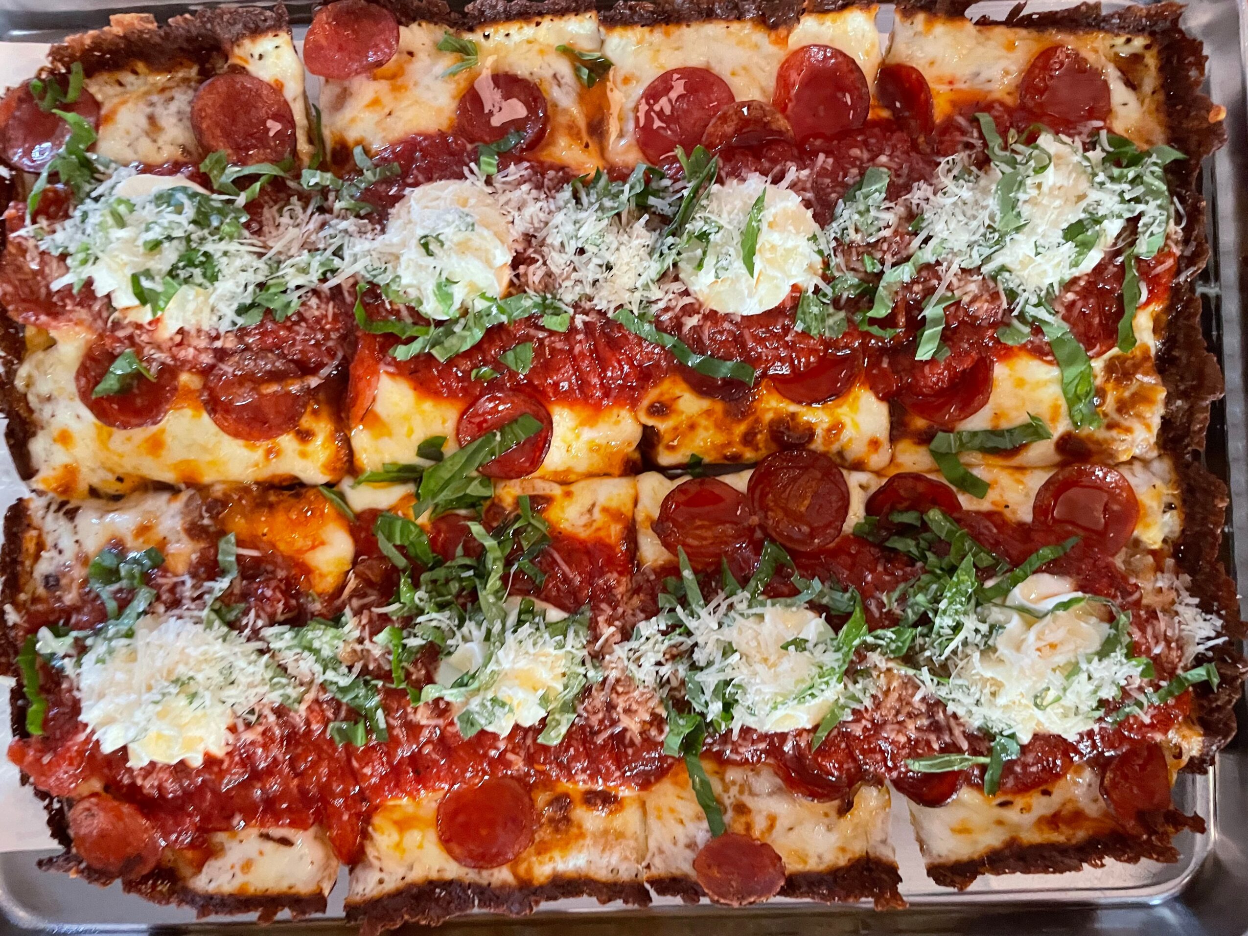 Close-up of a rectangular pizza topped with pepperoni, cheese, herbs, and grated cheese, on a tray.