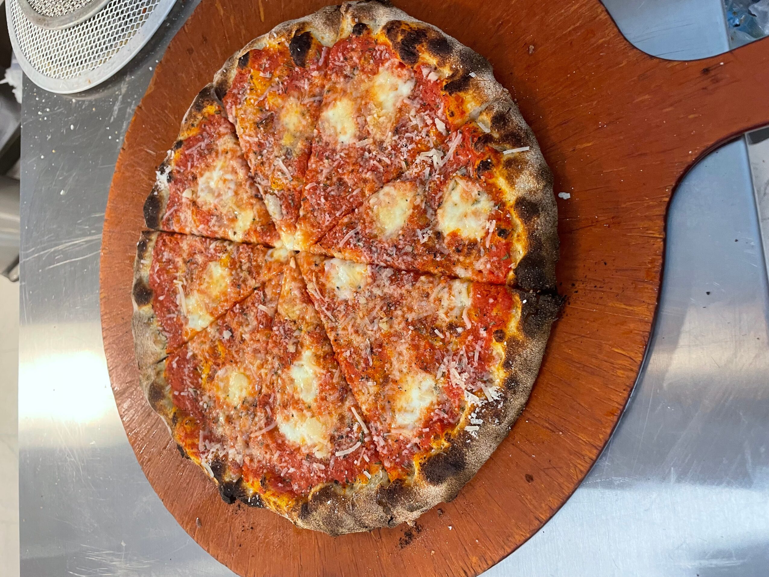 Cheese pizza on a wooden serving board, sliced into six pieces, with melted cheese and tomato sauce.