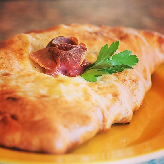 Close-up of a baked pastry with a piece of meat and a green parsley leaf on top, on a yellow plate.