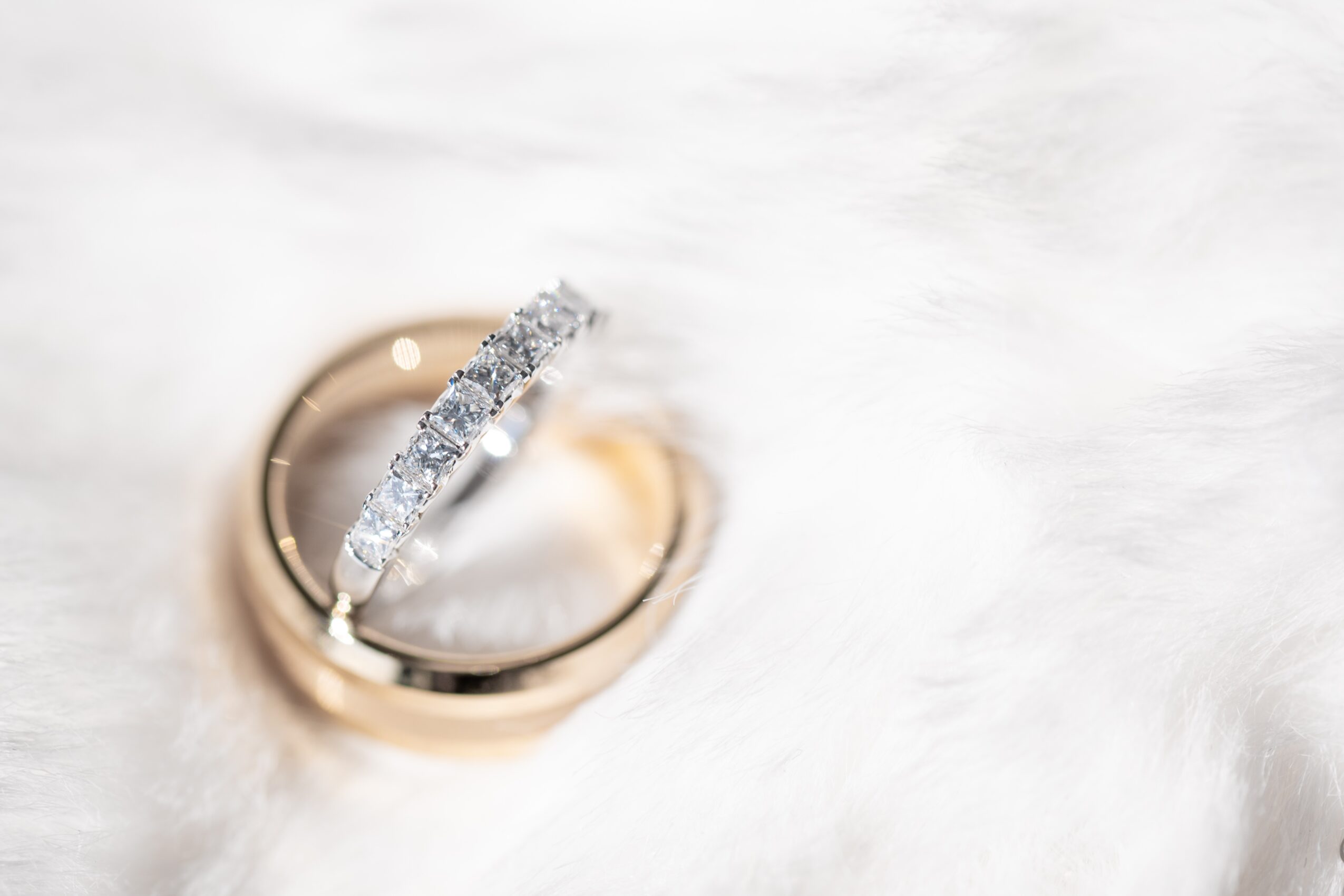 Two rings, one with diamonds, resting on white fur, one ring inside the other, close-up view.
