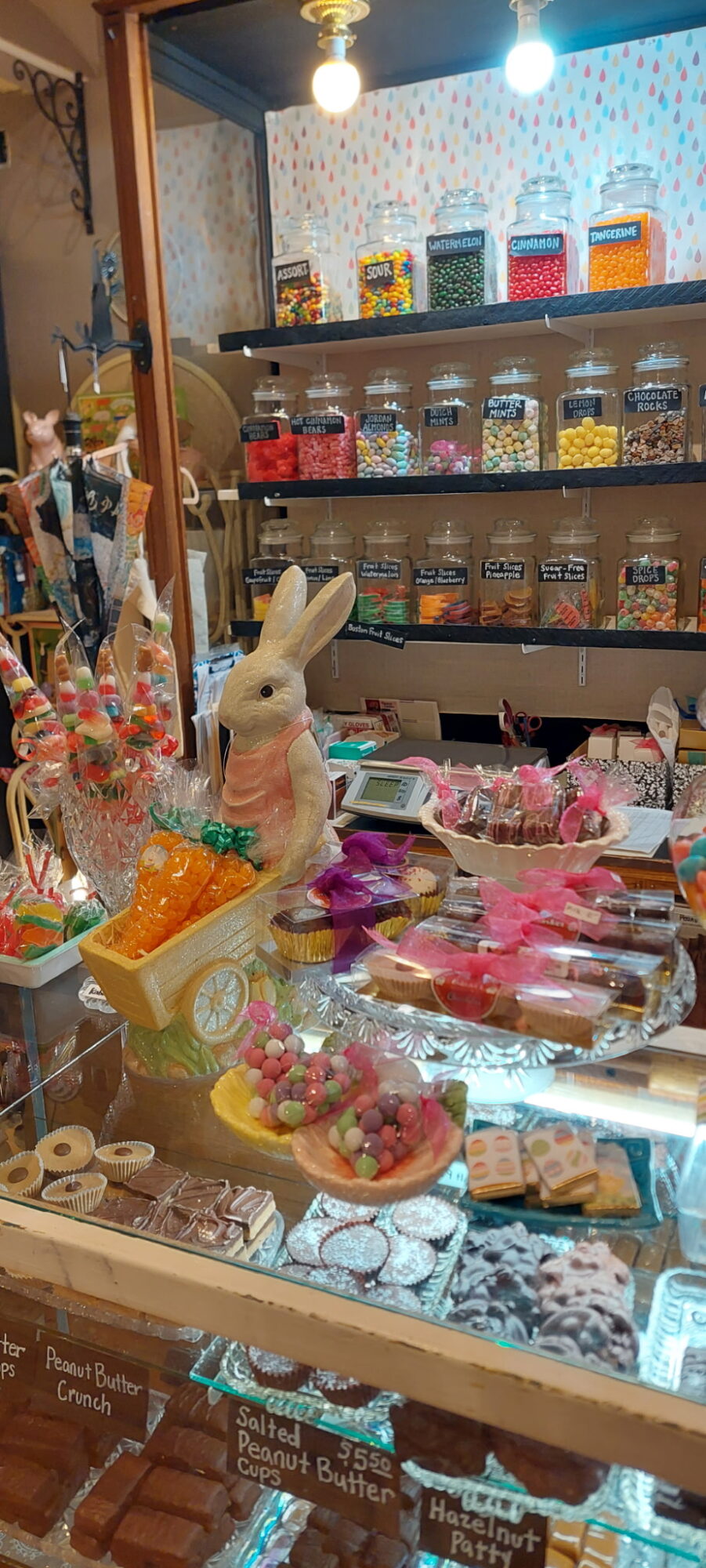 Display of colorful candies and sweets in jars and bowls on a table, with a rabbit figurine among the treats.