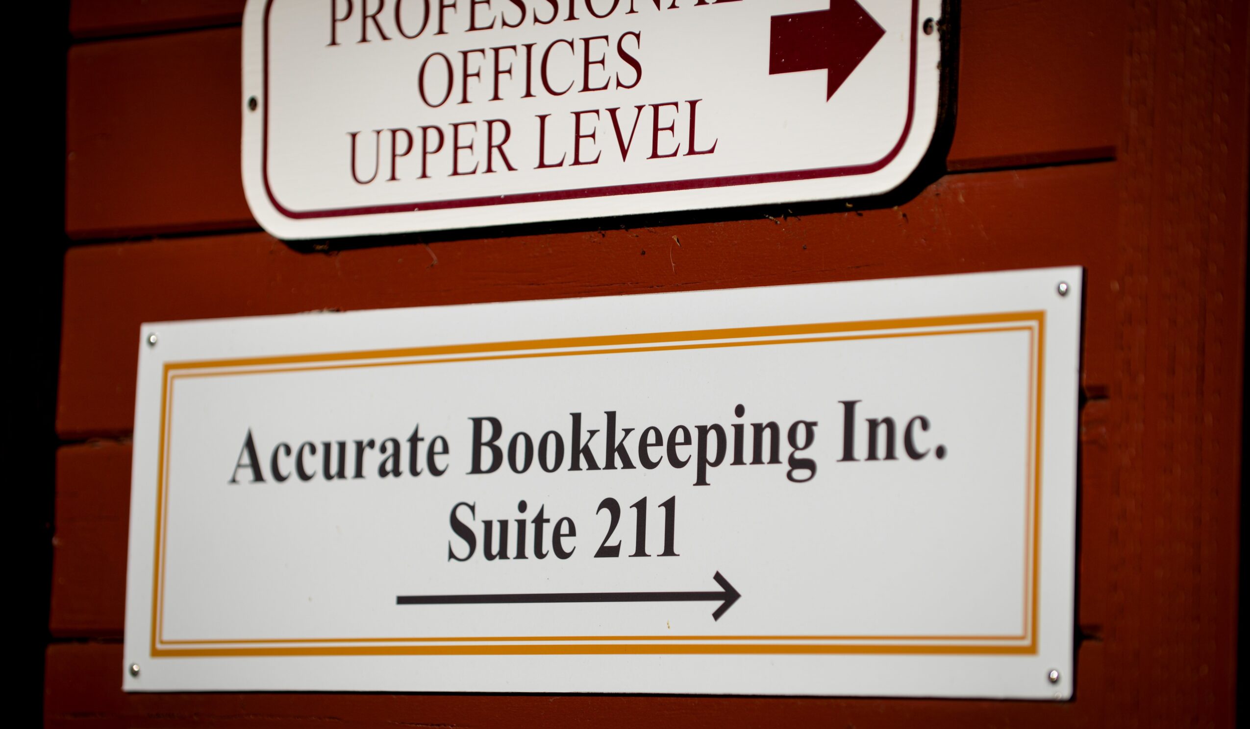Sign for Accurate Bookkeeping Inc. Suite 211 with an arrow pointing right, mounted on a wall.