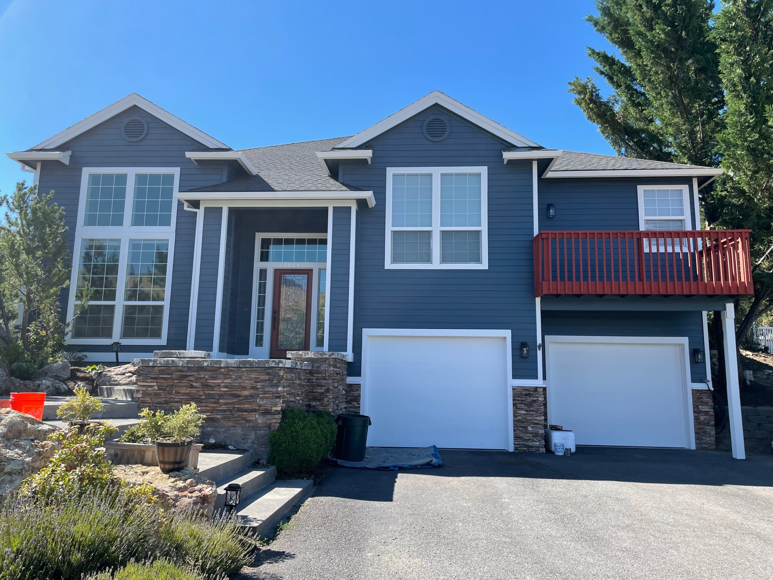 Two-story house with blue siding, large windows, a red balcony, and a garage, under a clear blue sky.