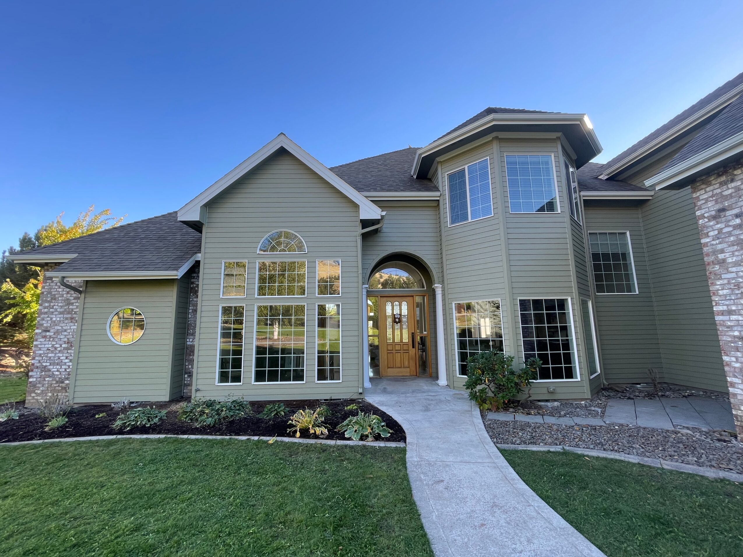 Front view of a large house with multiple windows, a curved walkway, and a well-maintained lawn under a clear blue sky.