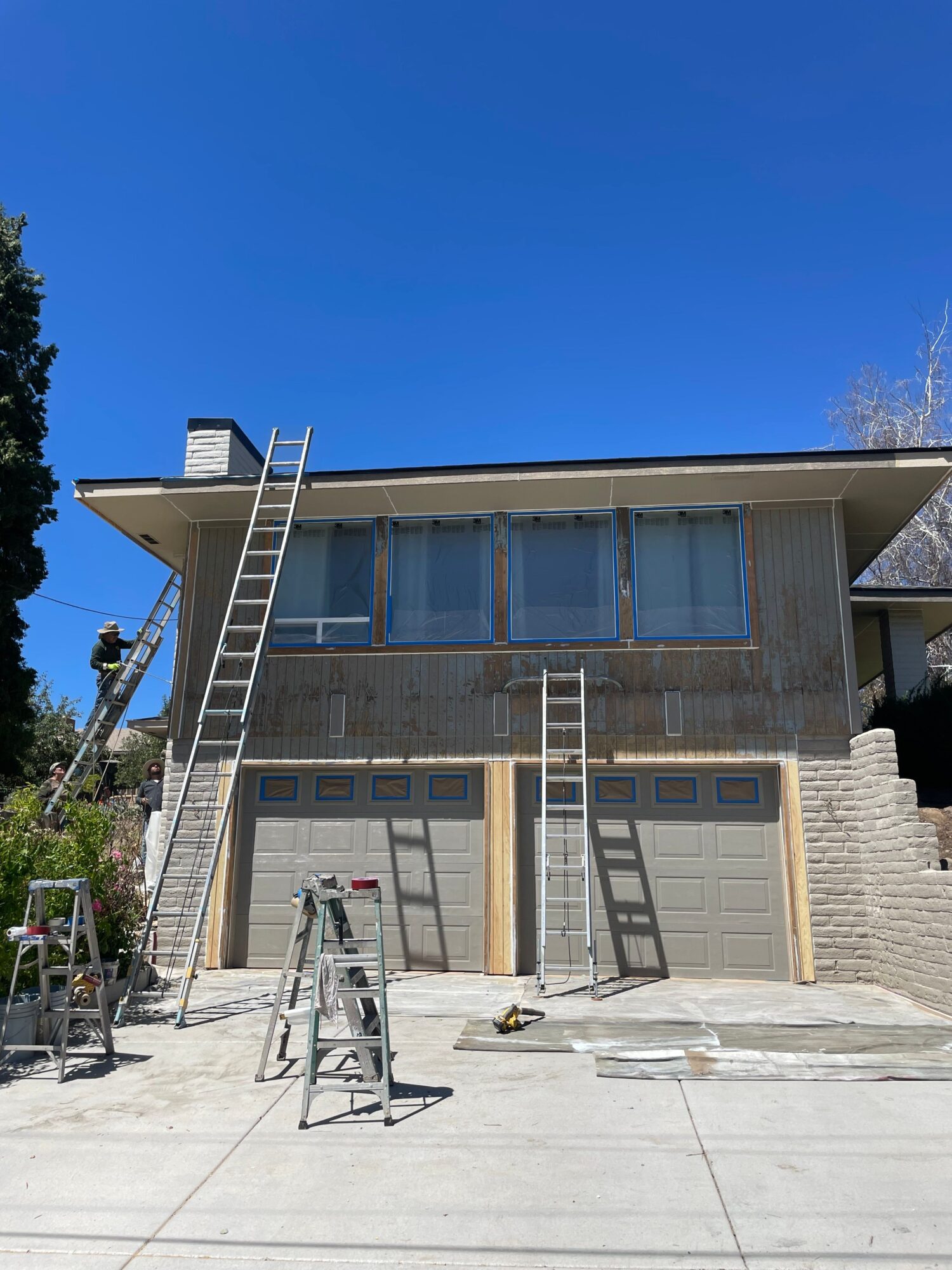 Building with large glass windows, metal stairs, and a ladder outside, under a clear blue sky.
