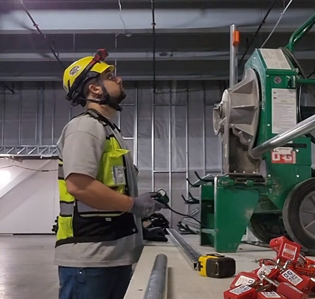 Worker in safety gear operating a large green industrial machine in a warehouse setting.