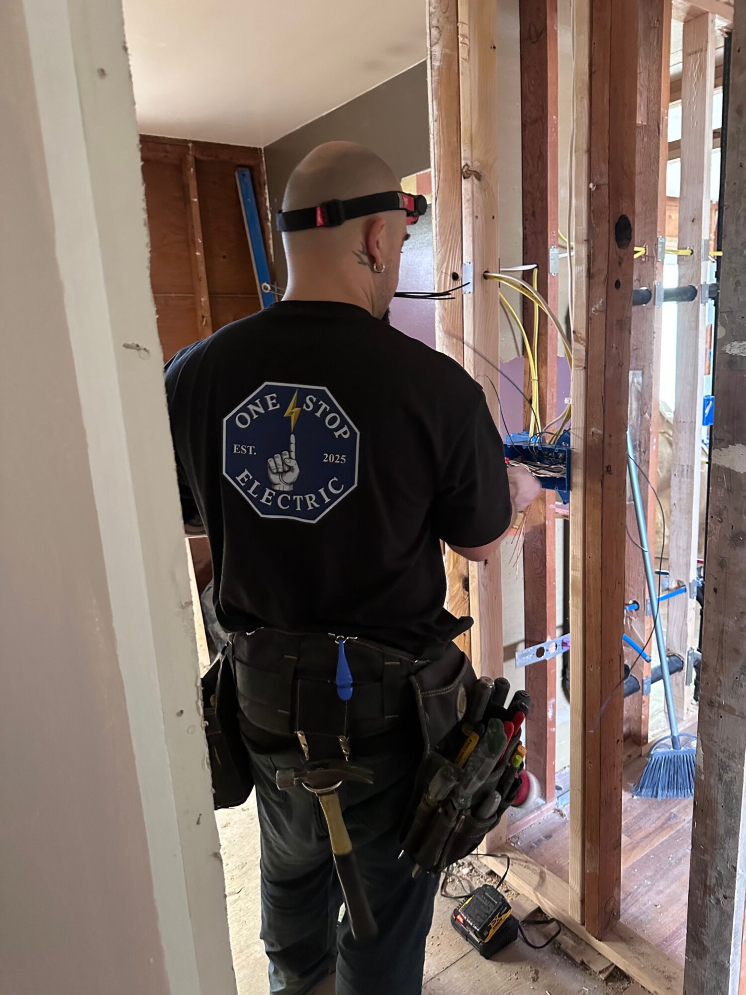 Construction worker wearing a black shirt with a logo, safety glasses, and a harness, working on a wooden frame.