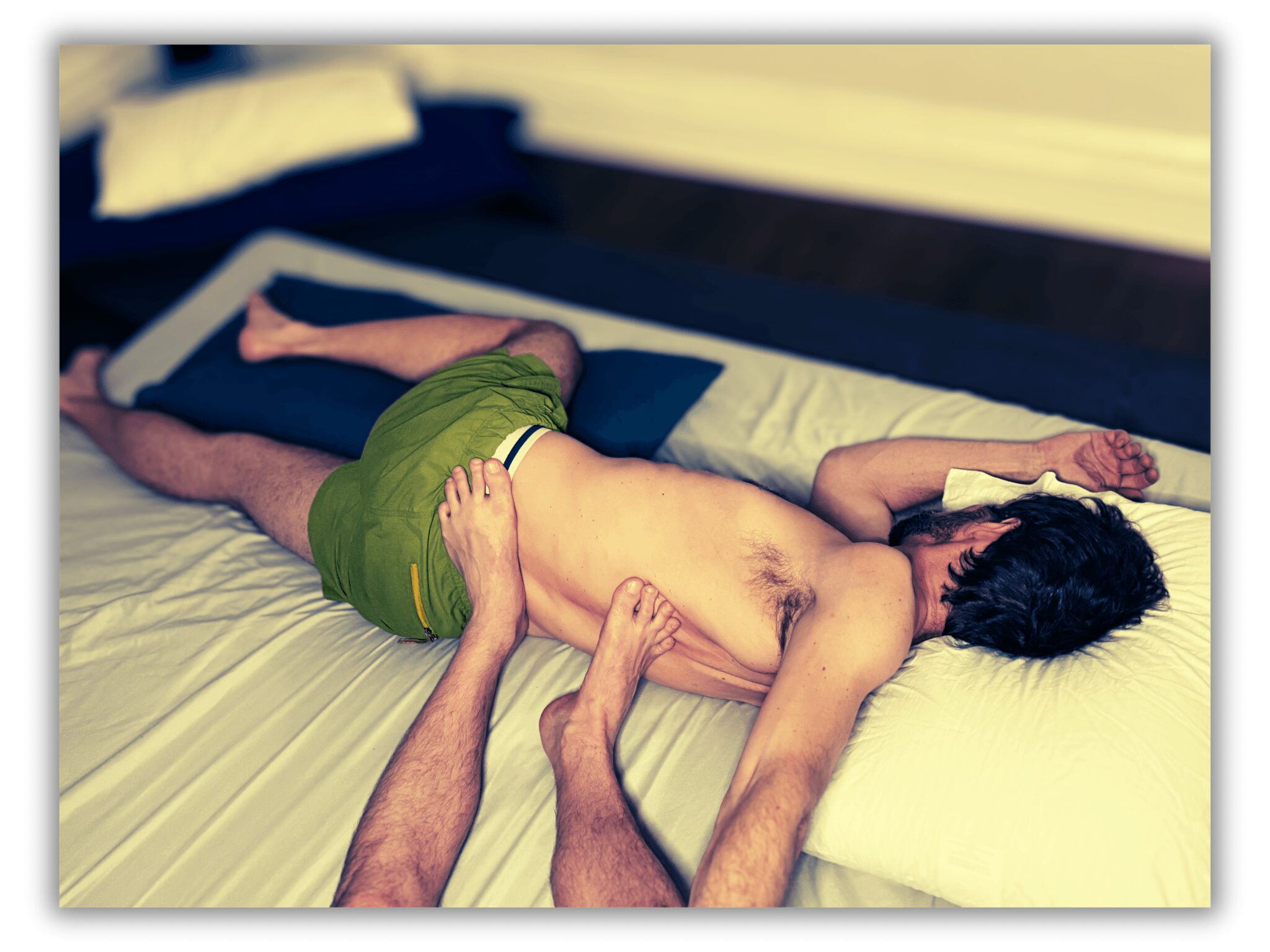 Two people lying on a bed, one on top of the other, with a pillow and blanket nearby.