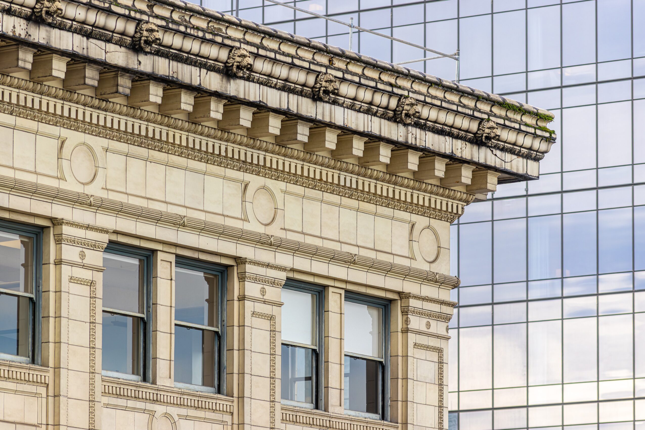 Close-up of a historic building's ornate stone facade with modern glass building reflected in the background.