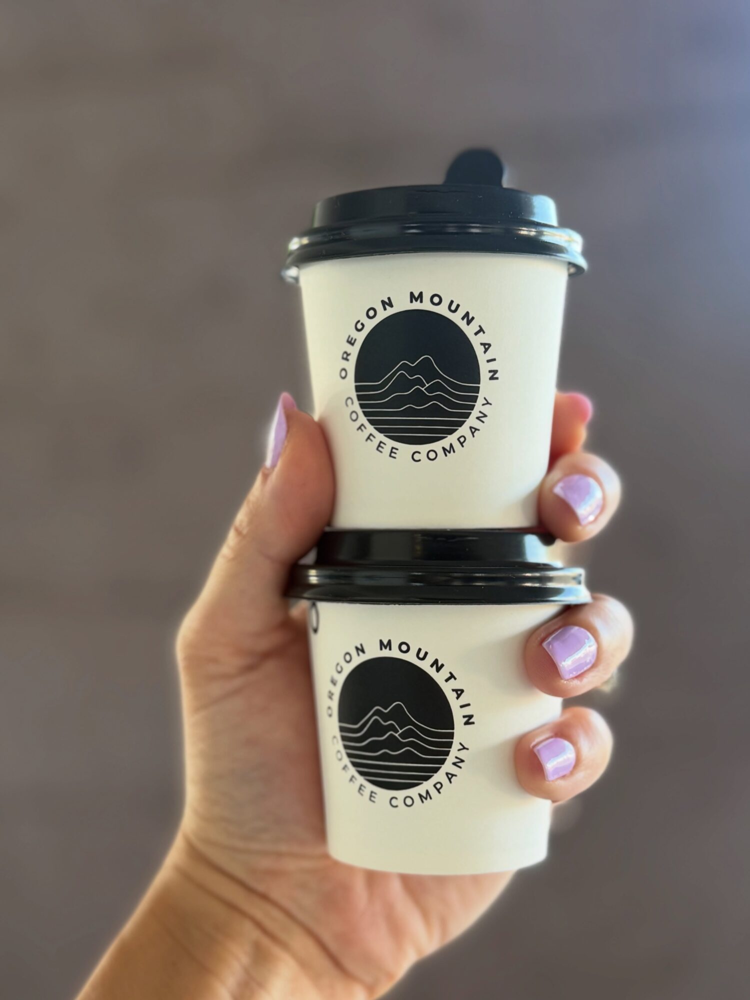 Person holding two coffee cups with logo, one above the other, against a plain background.