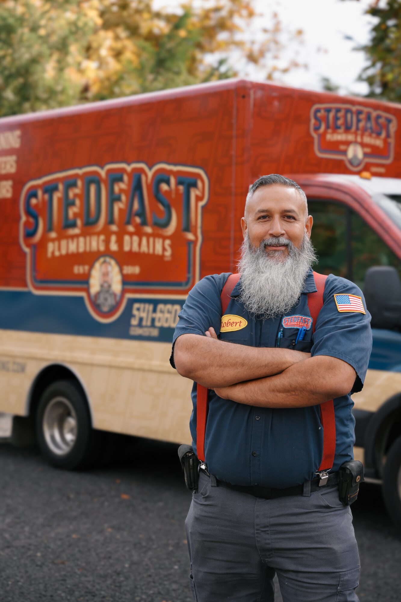 Man with a beard in a uniform standing with arms crossed in front of a food truck with Stedfast logo.