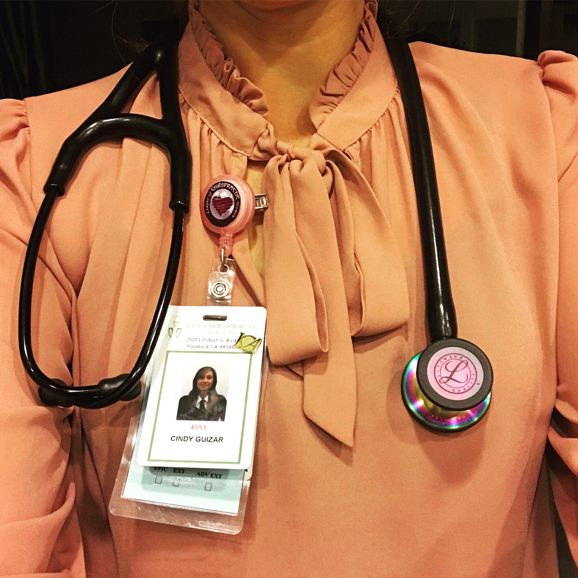 Person wearing a pink blouse with a bow, stethoscope, and ID badge, cropped at shoulders and neck.