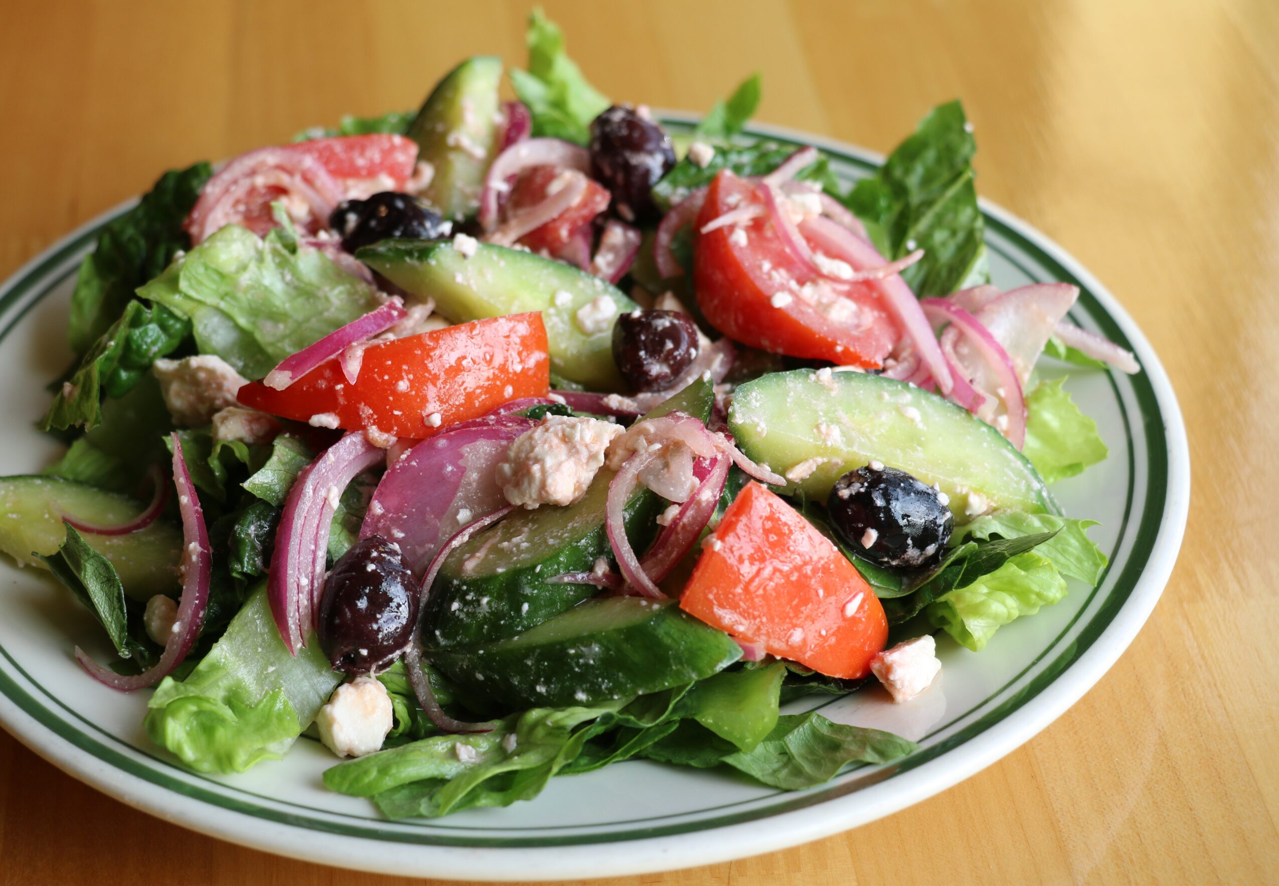 Fresh vegetable salad with cucumbers, tomatoes, red onions, black olives, and leafy greens on a white plate