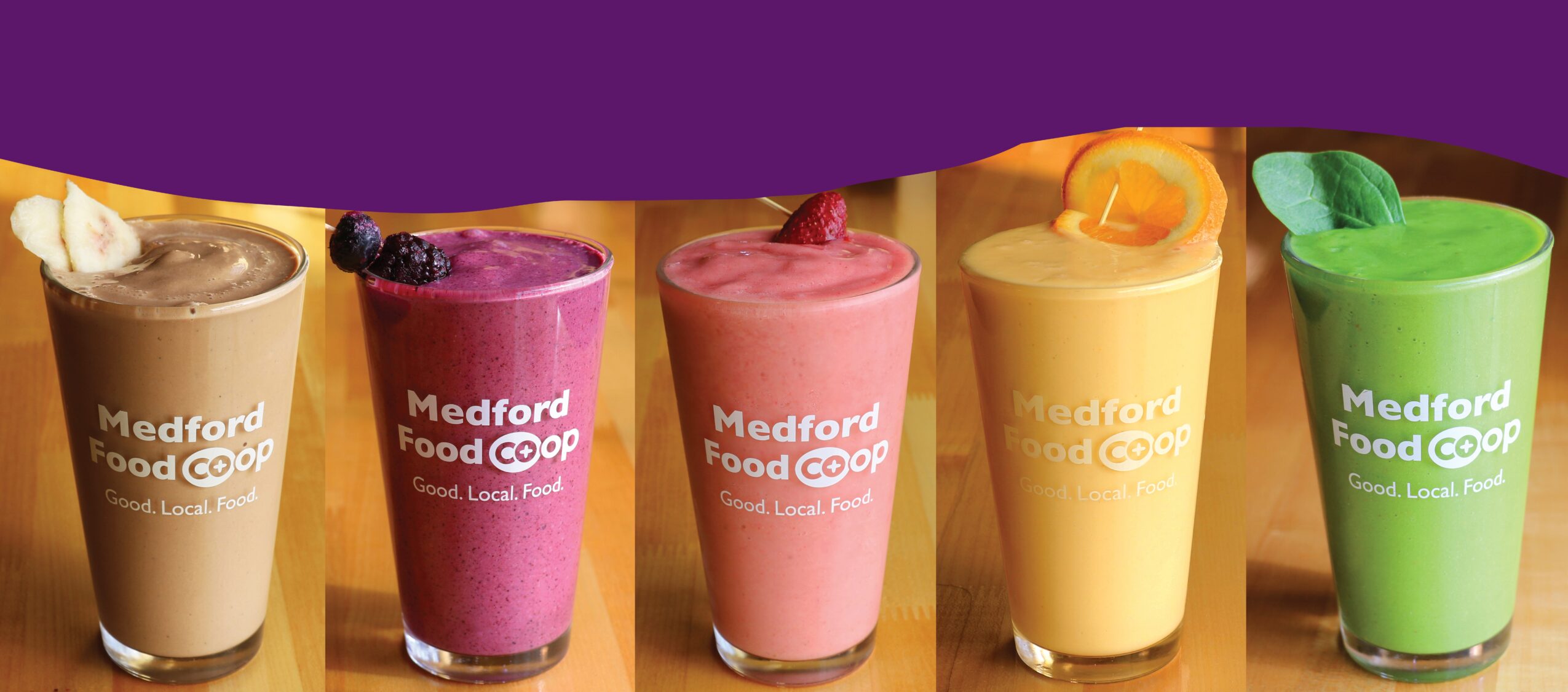 Five colorful smoothies in cups with Medford Food Co-op labels, arranged in a row against a purple background.