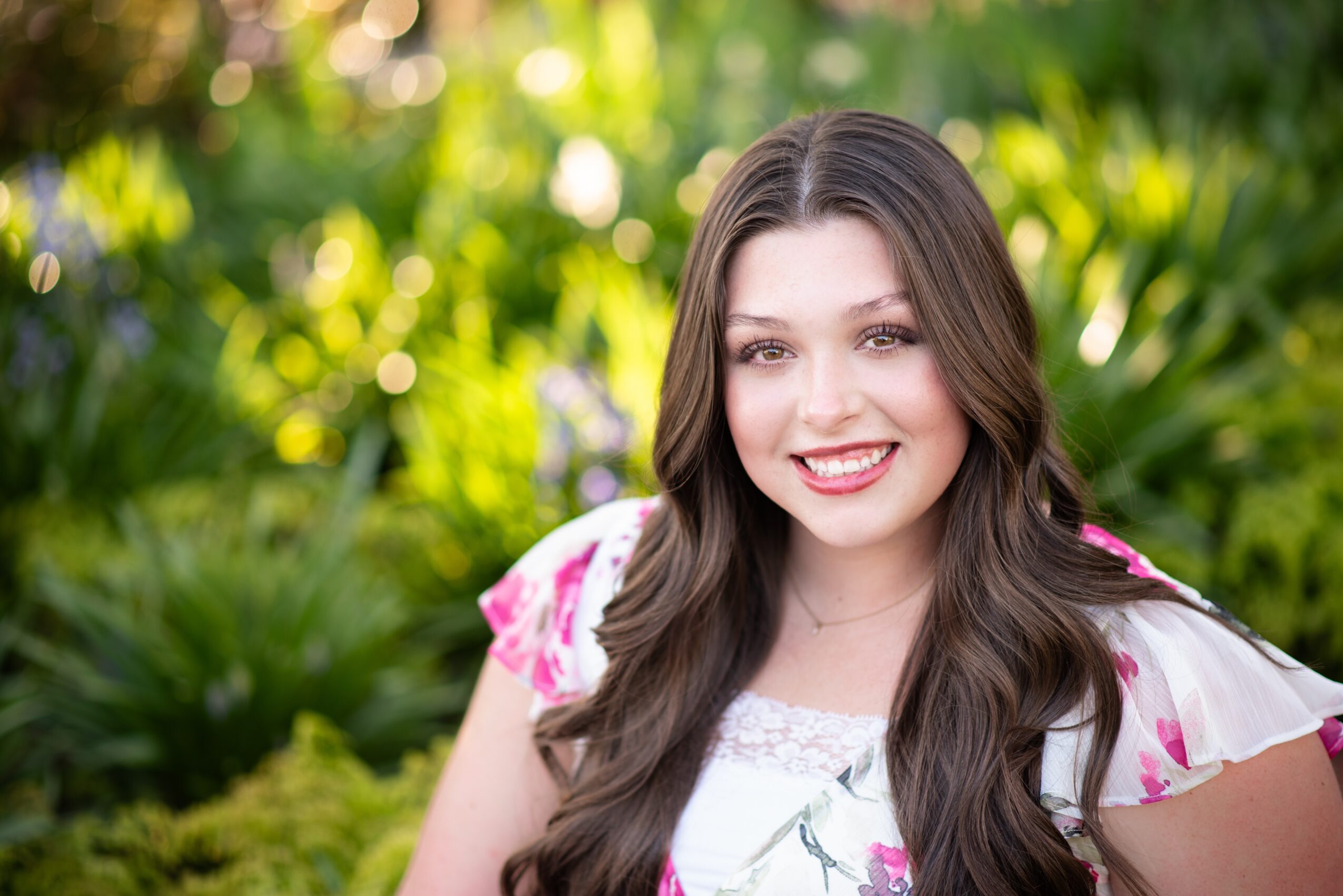 Young woman with long dark hair smiling outdoors with green foliage background