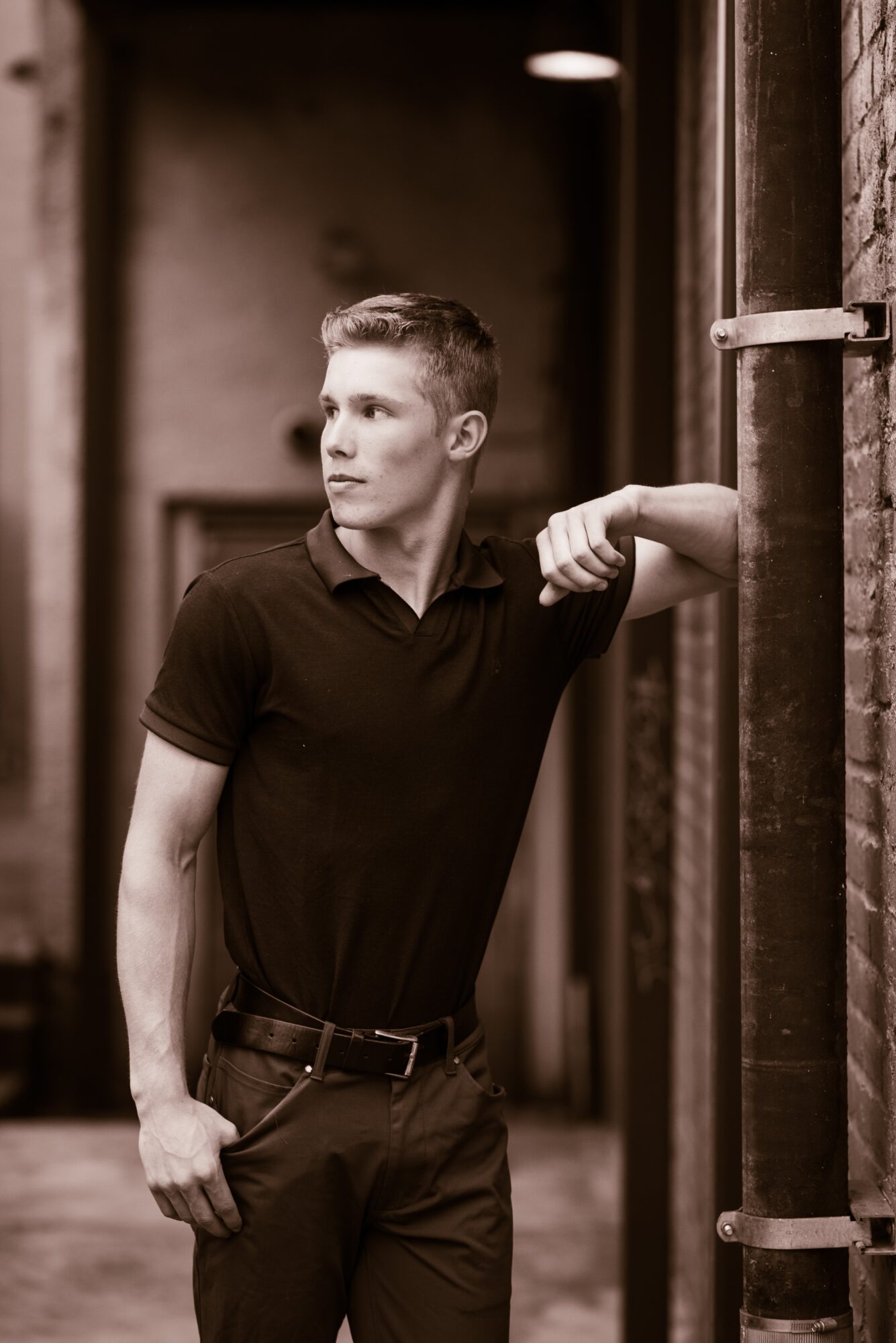 Young man with short hair in a black polo shirt leaning against pipes in an industrial setting.