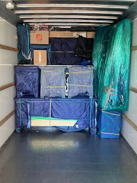 Packed storage unit with boxes, bags, and a large plastic sheet, viewed from the front. Word count: 20.