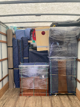Storage unit filled with packed boxes, bags, and furniture wrapped in plastic, stacked tightly inside a container.