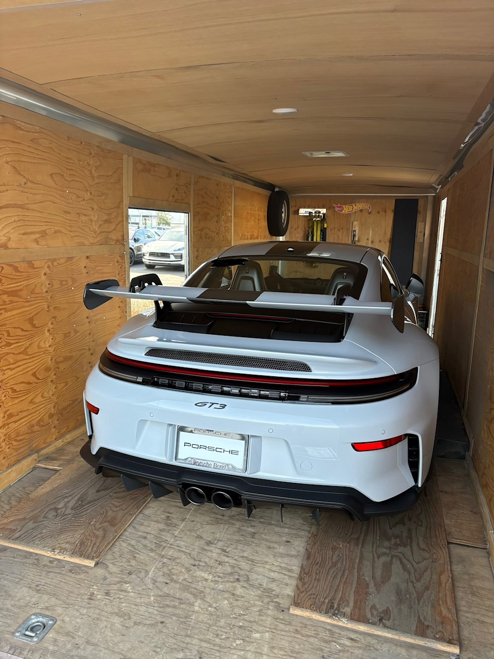 White sports car with a large rear wing parked inside a wooden-walled garage.