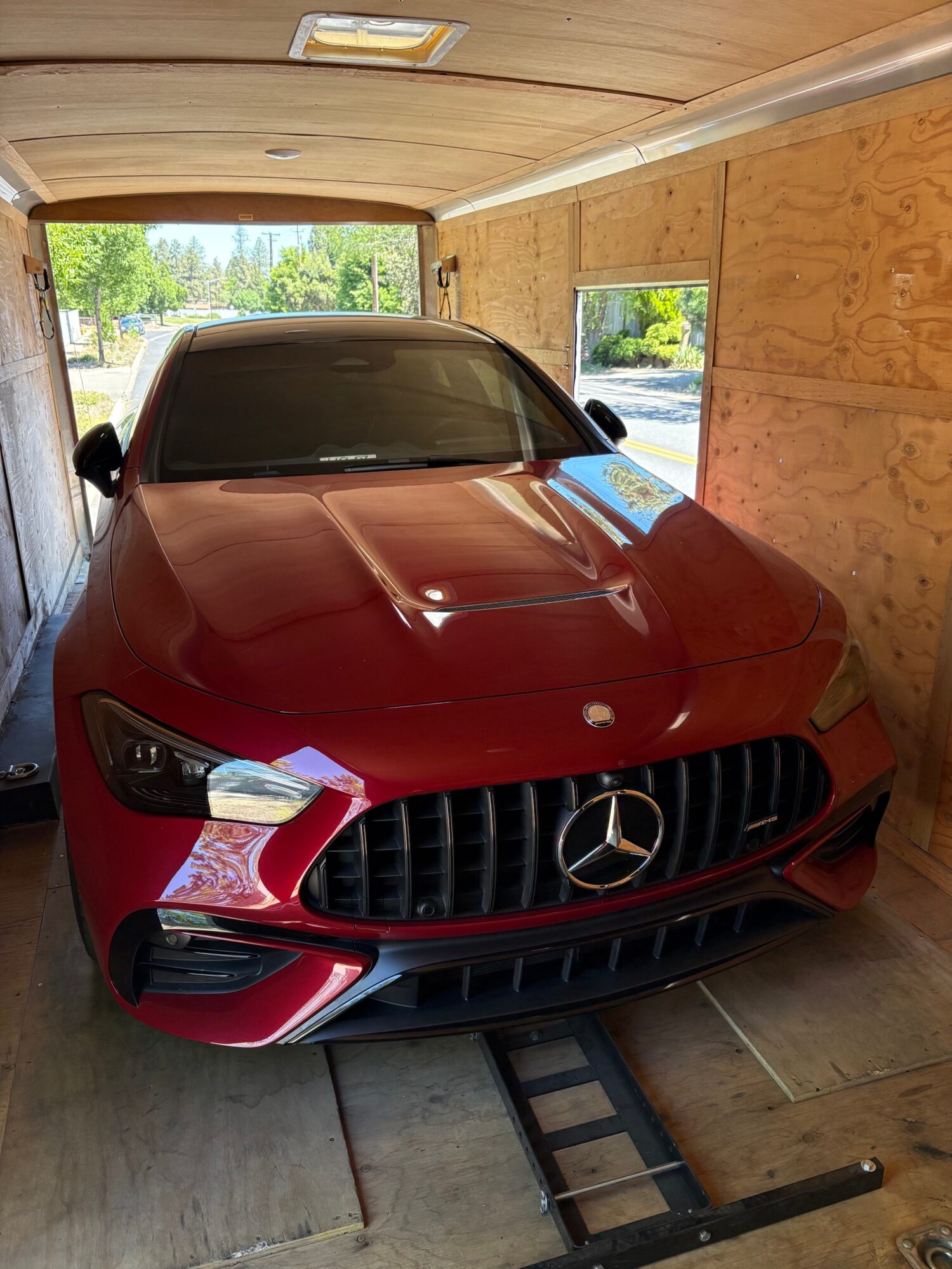 Red Mercedes-Benz car parked inside a wooden garage with windows, viewed from the front, with a ramp in front.