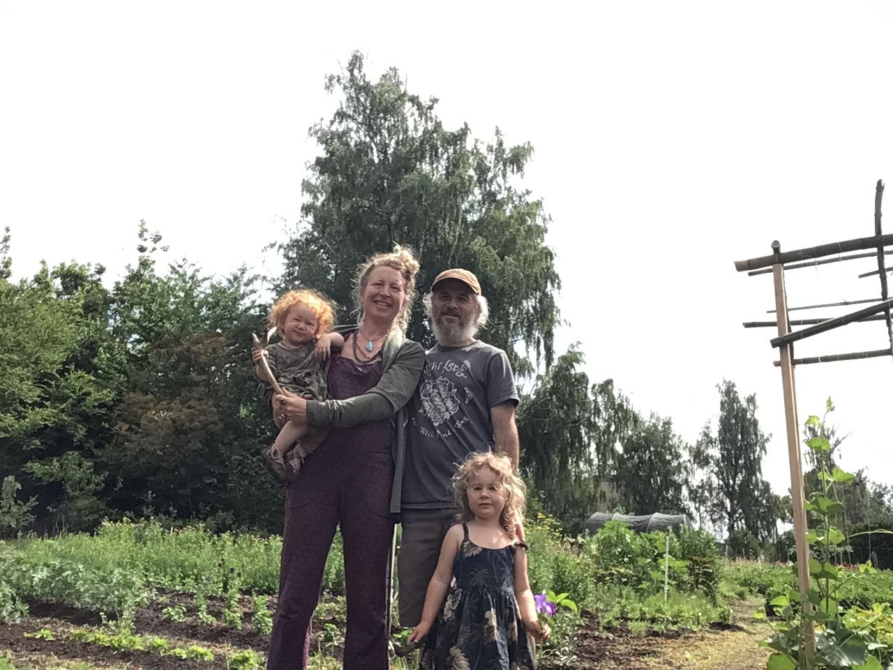 Four people standing outdoors in a garden with trees and plants, smiling and posing for the photo.