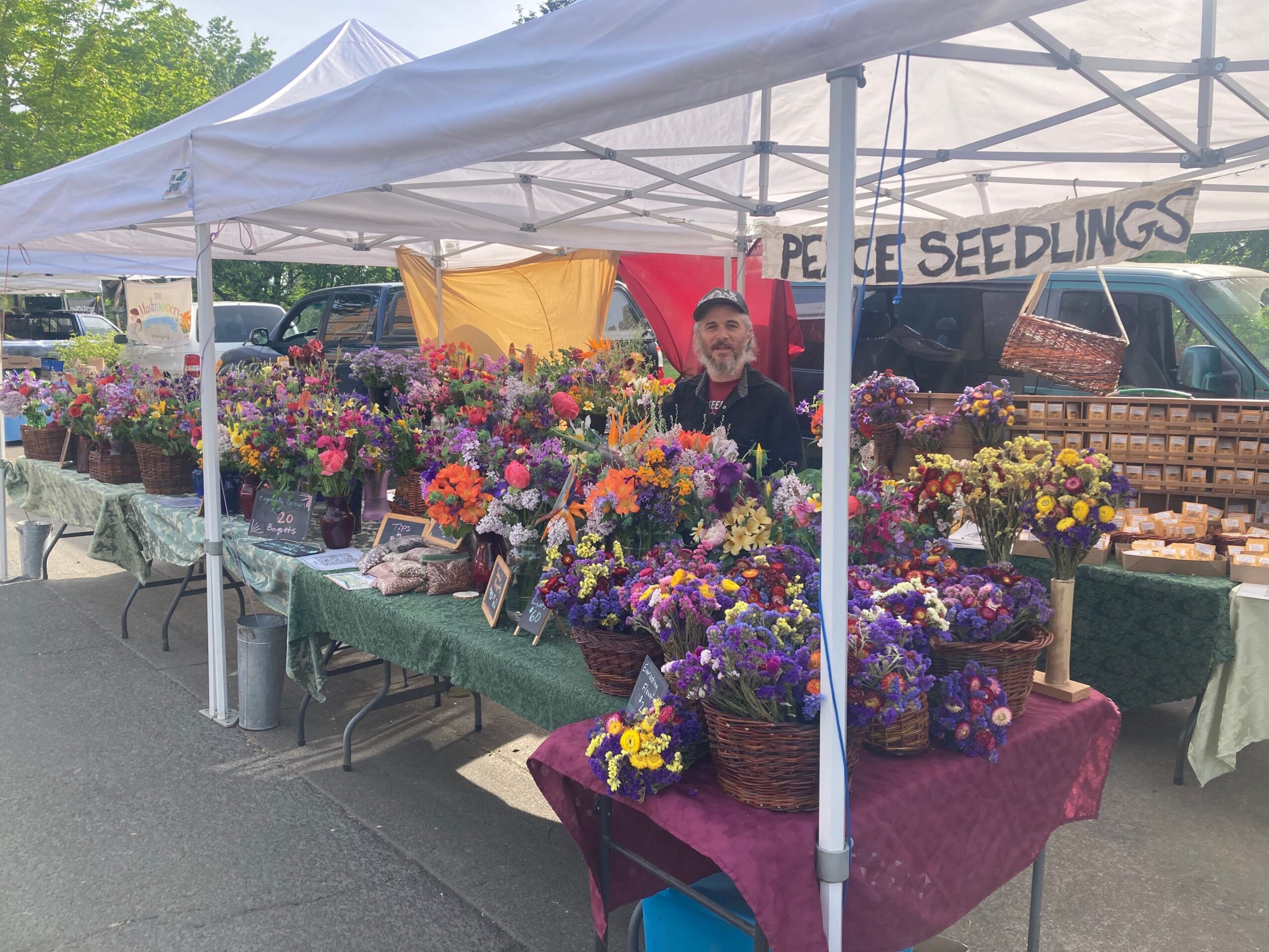 Market stall with colorful flowers and umbrellas, with a person in a yellow shirt in the background.