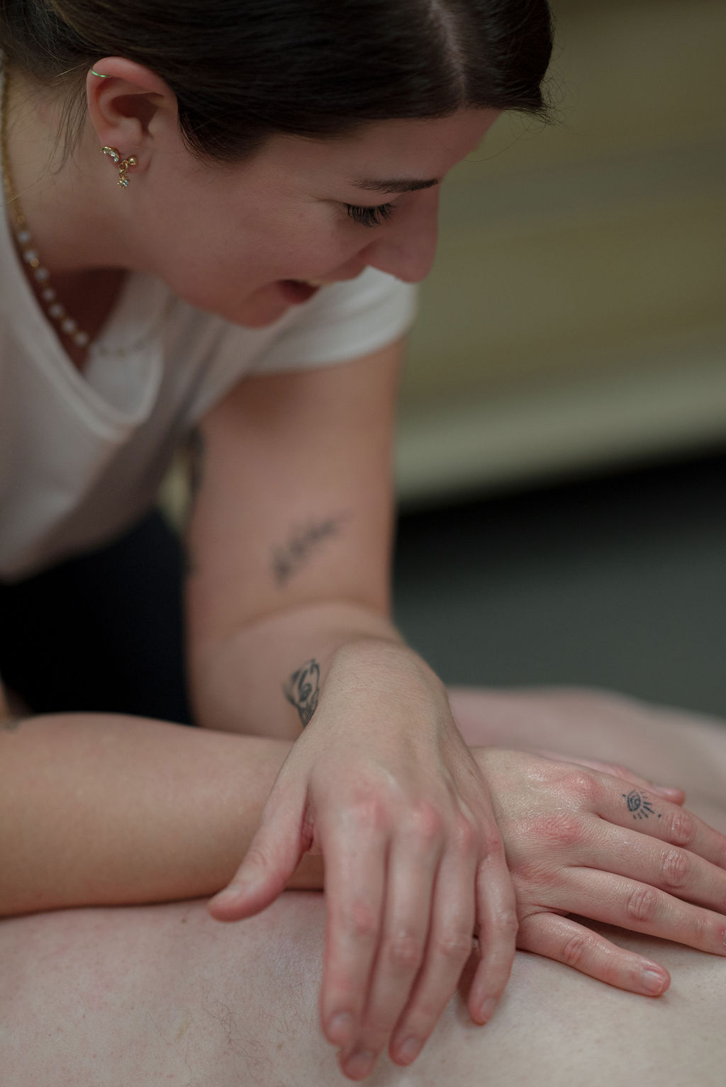 Close-up of a woman with dark hair, wearing a white shirt, gently touching a person's arm.