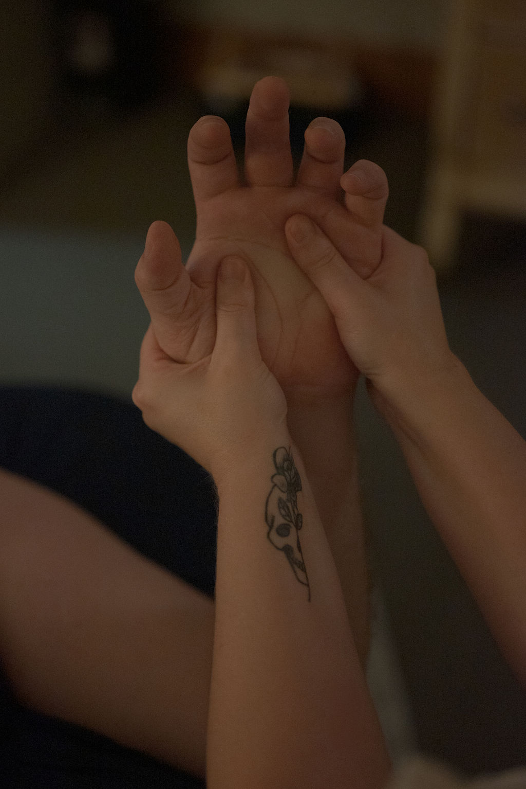 Two hands holding each other, one with a tattoo on the forearm, in a close-up shot.