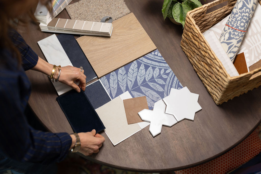 Person arranging fabric samples and color swatches on a table, with a basket of textiles nearby.